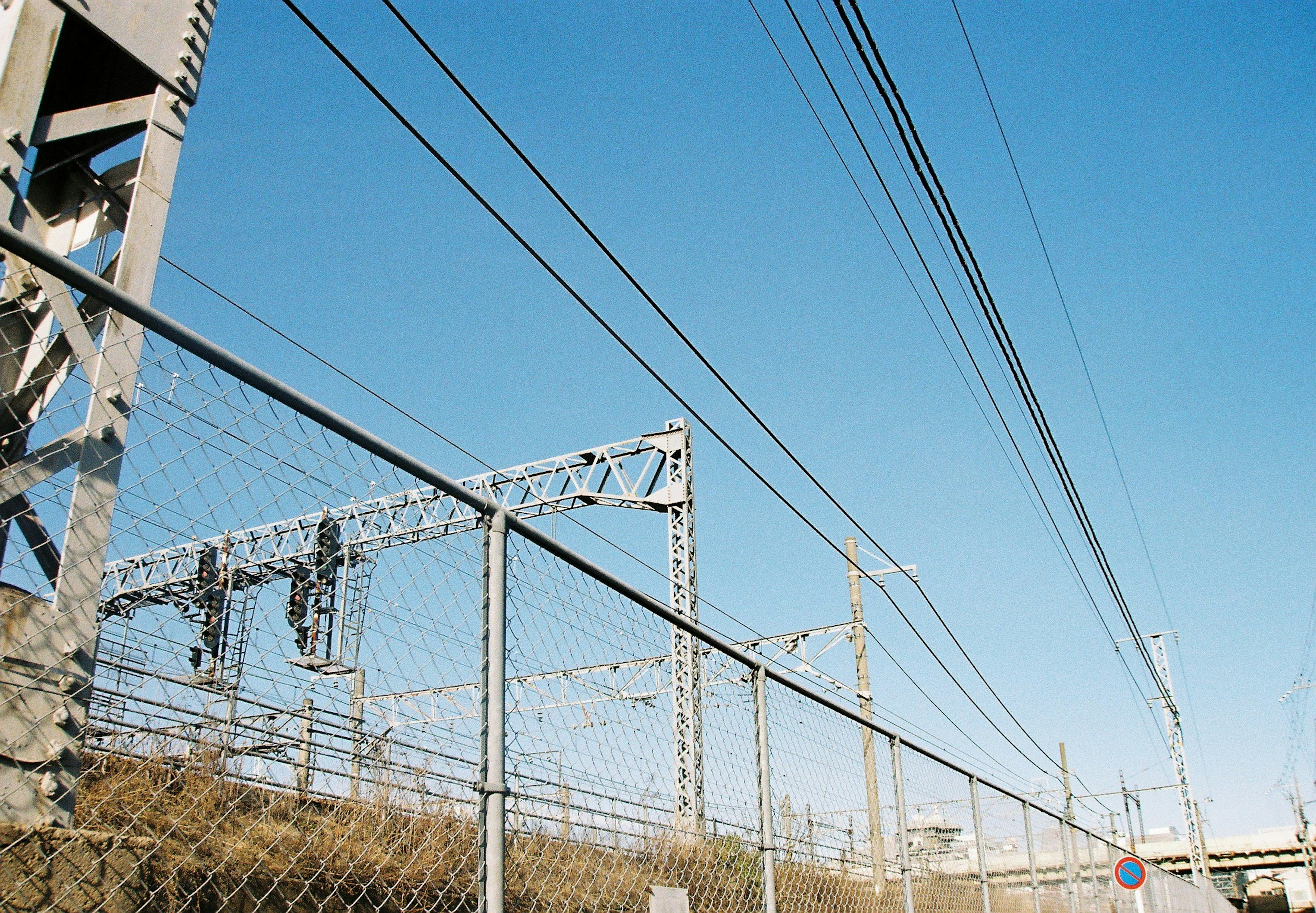 View of railway overhead lines and fence under a clear blue sky