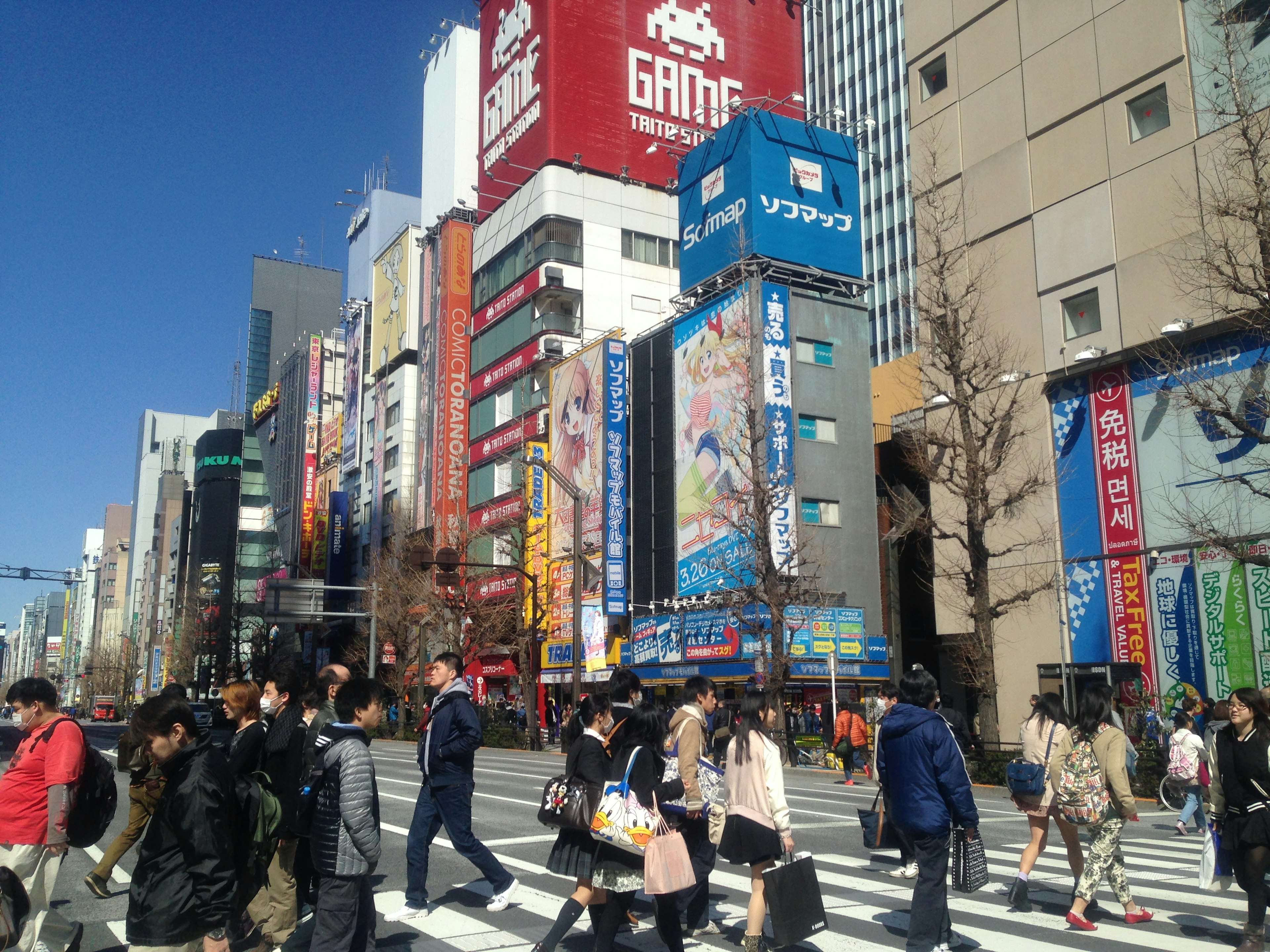 賑やかな都市の交差点に集まる人々と色とりどりの看板が特徴の風景