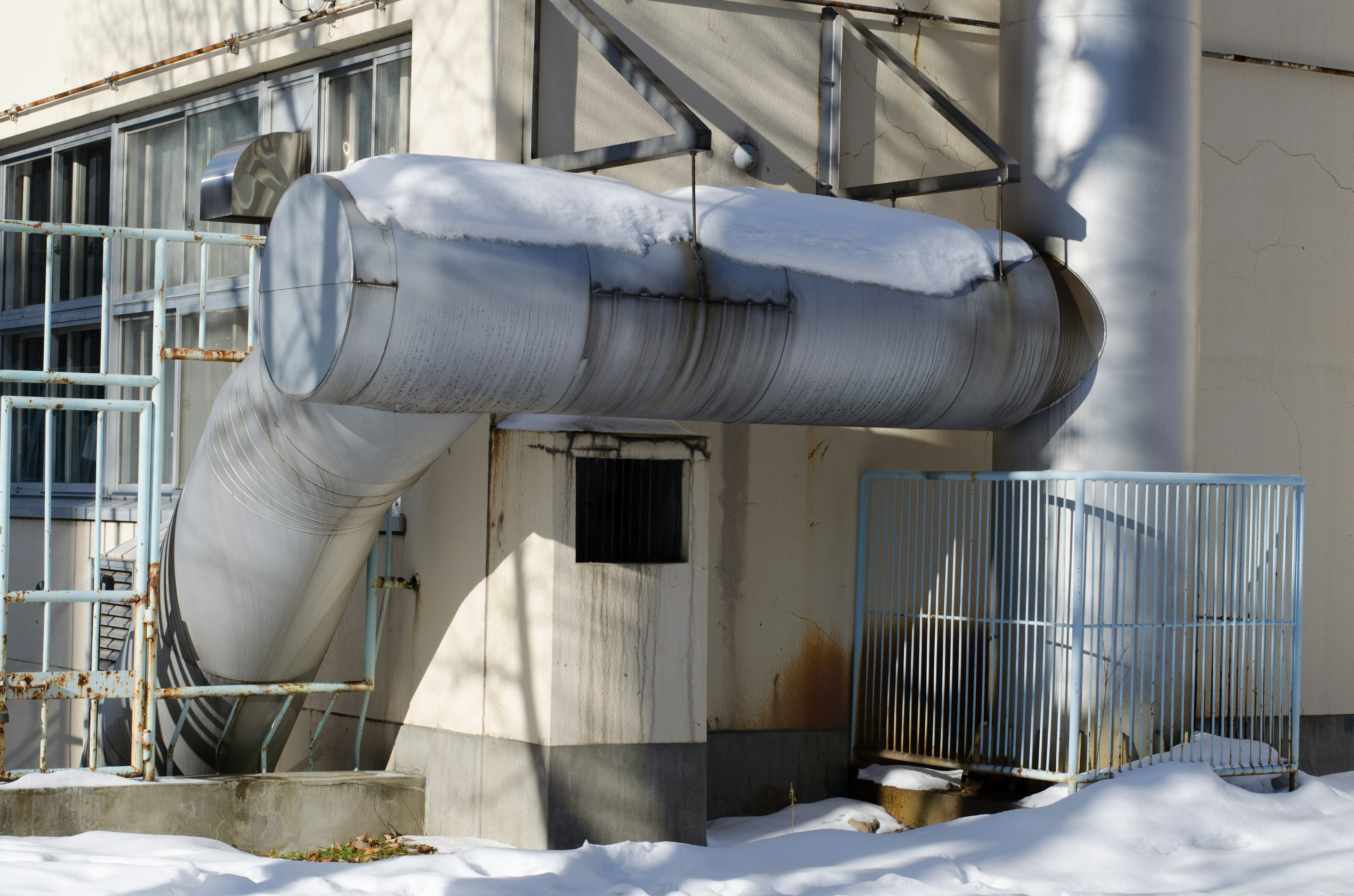 Metallrohr und Tor an der Außenwand einer mit Schnee bedeckten Fabrik