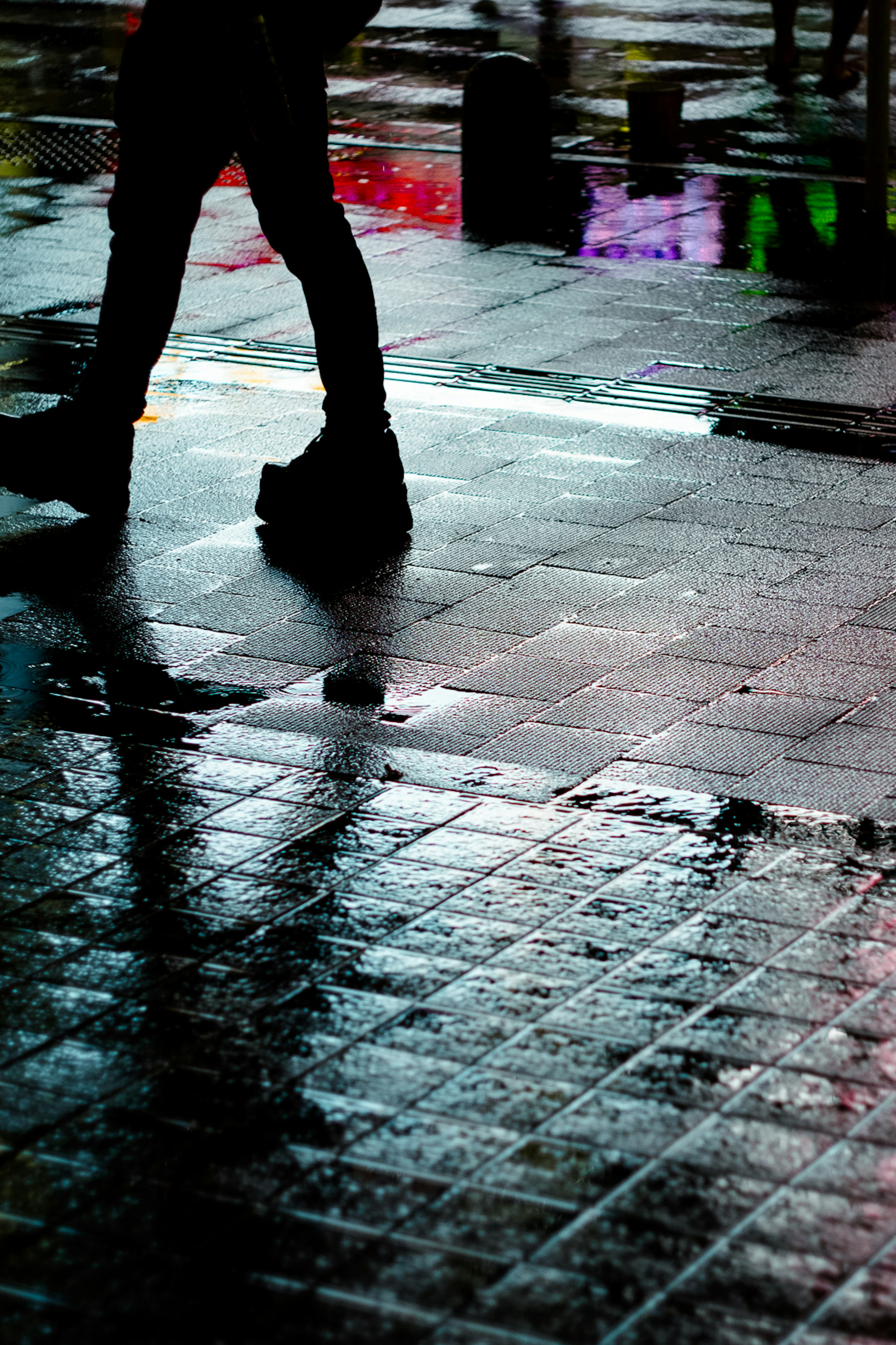 Silhouette of a person walking on a rain-soaked street with reflections