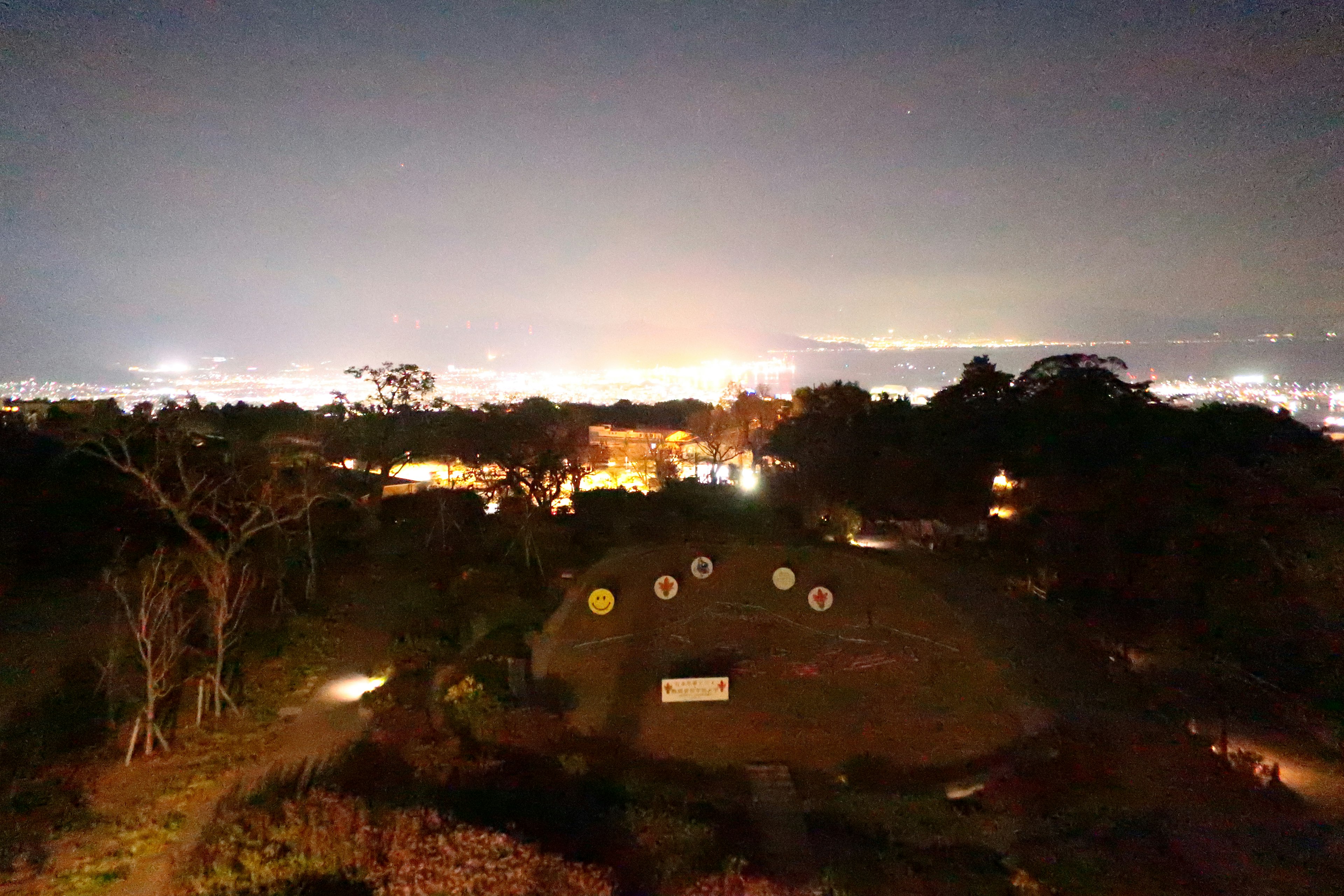 Vue nocturne avec des lumières de la ville et des arbres verts présentant des objets circulaires