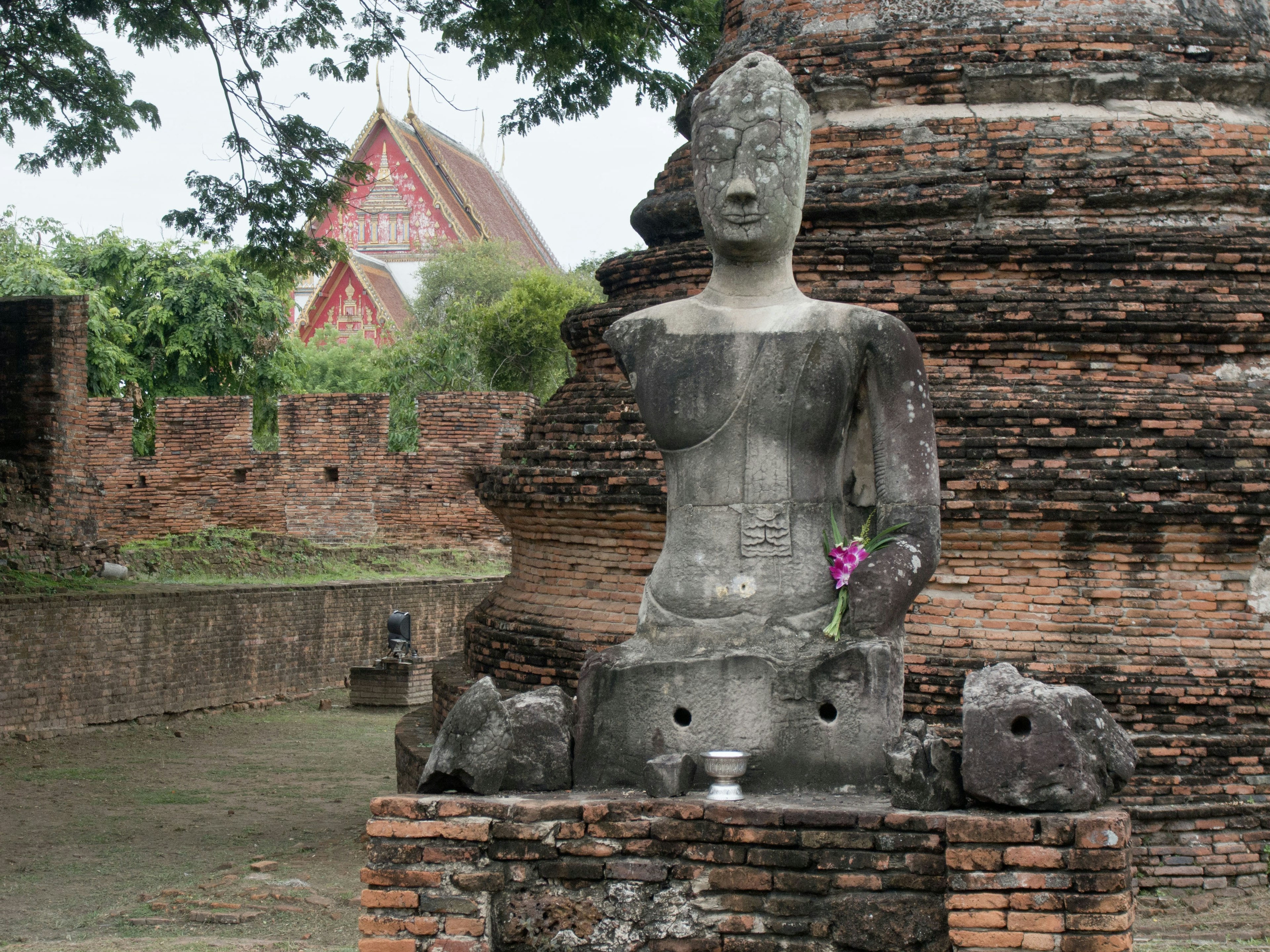 Antike Buddha-Statue neben Ziegelruinen mit einer Blumenopfergabe