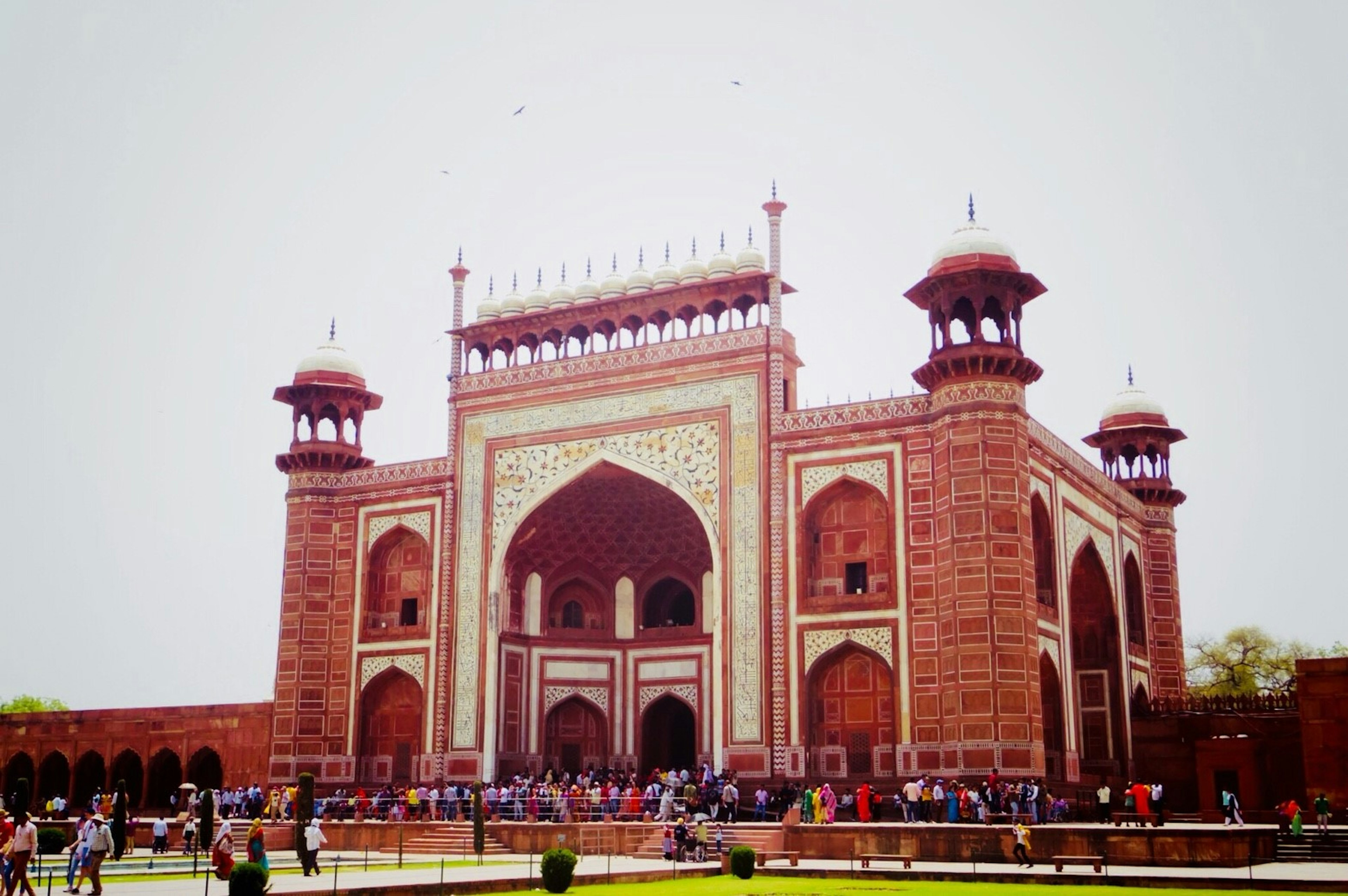 Entrée du Taj Mahal avec une architecture en briques rouges et des arches de nombreux touristes