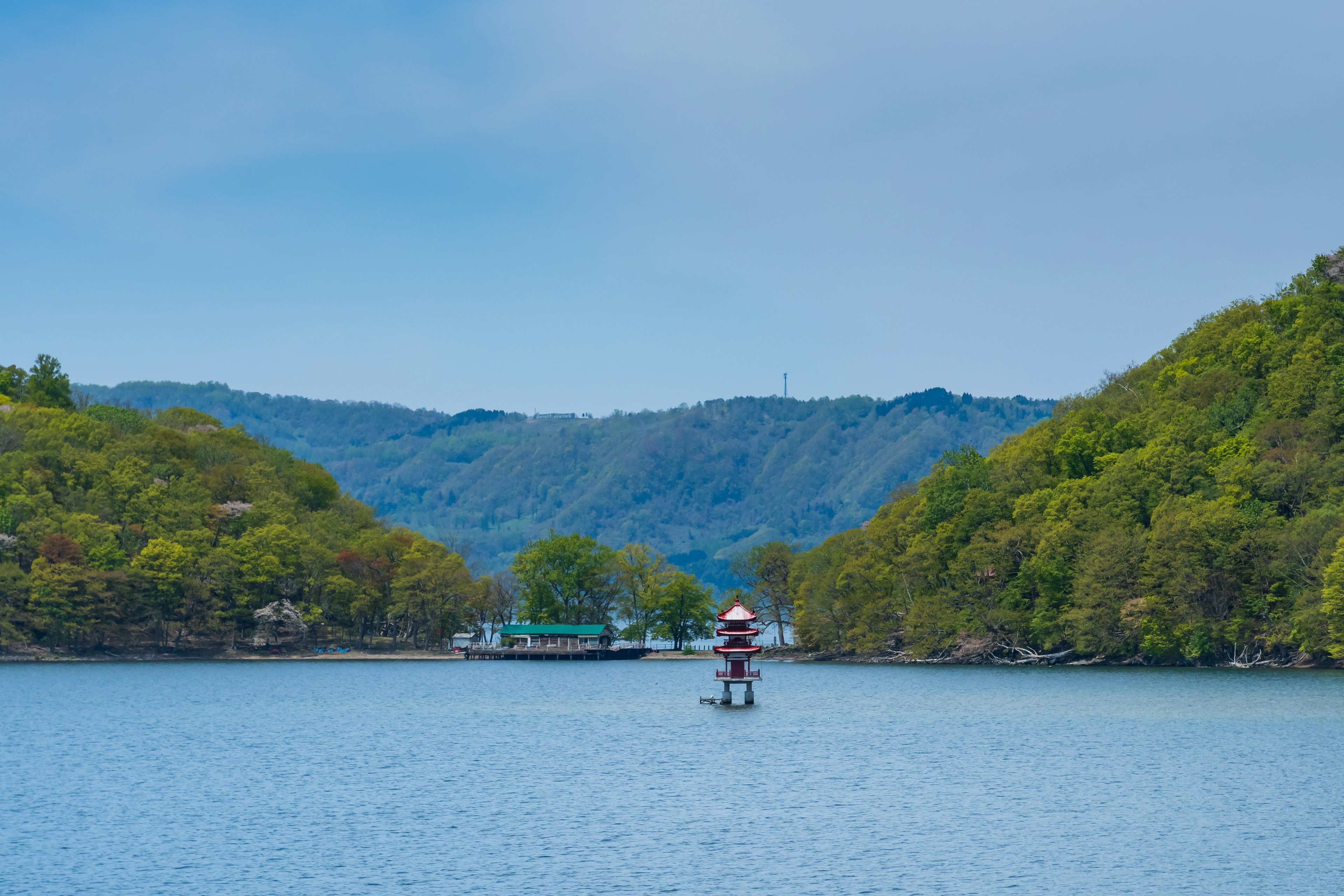 静かな湖に立つ灯台と緑豊かな山々