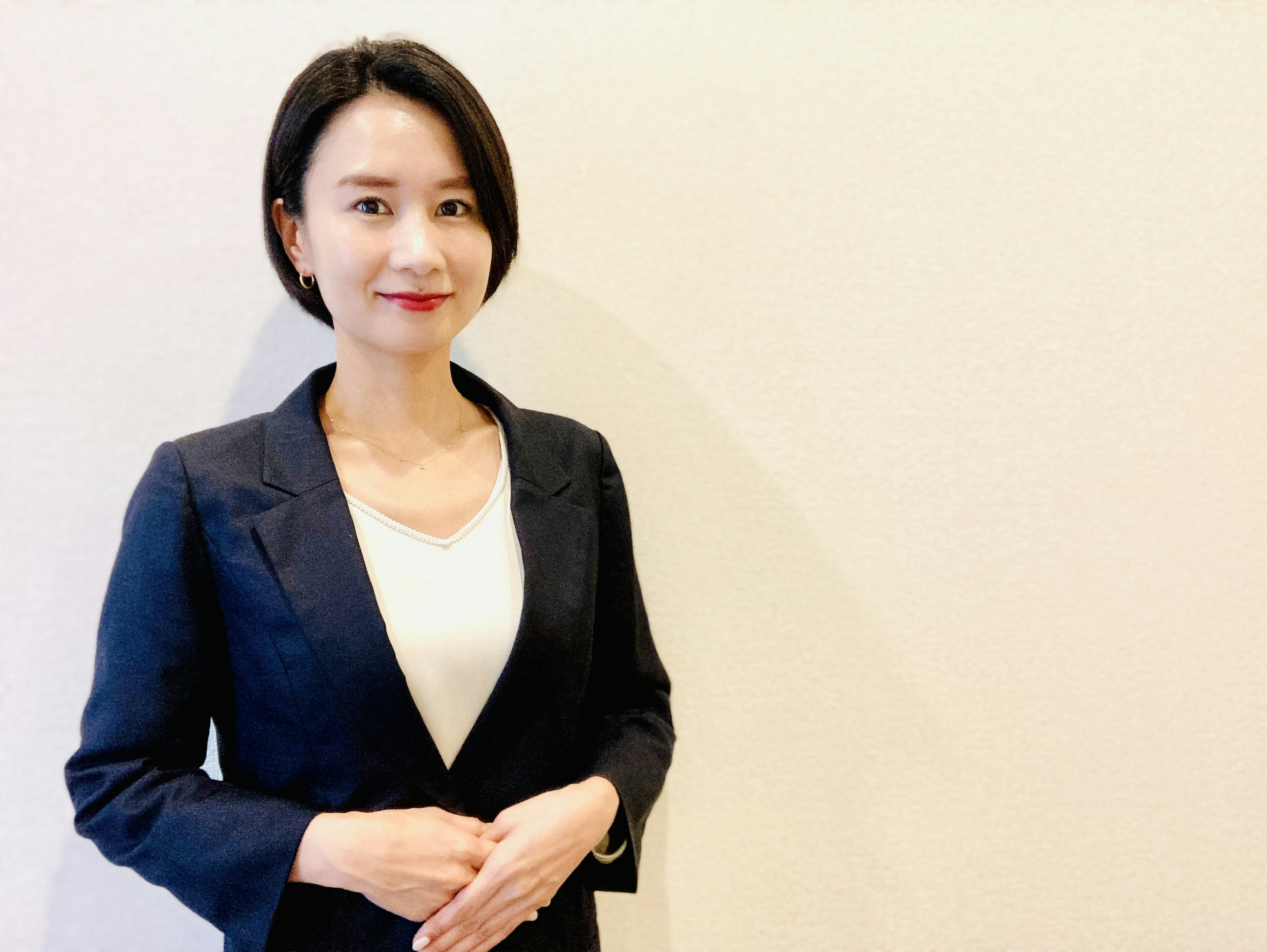 A woman in a suit standing with a smile against a bright background