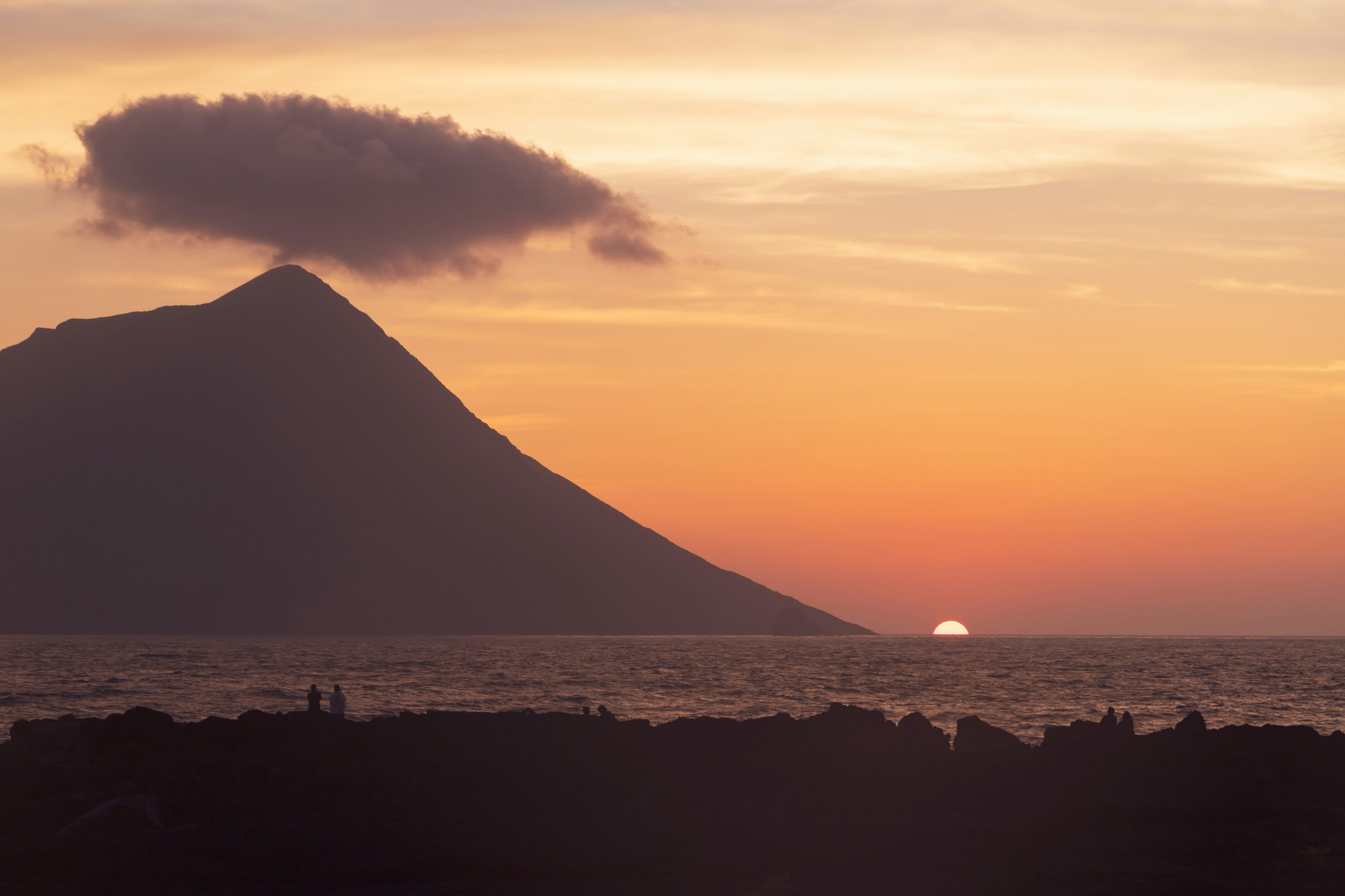 Silhouette of a mountain against a sunset over the sea