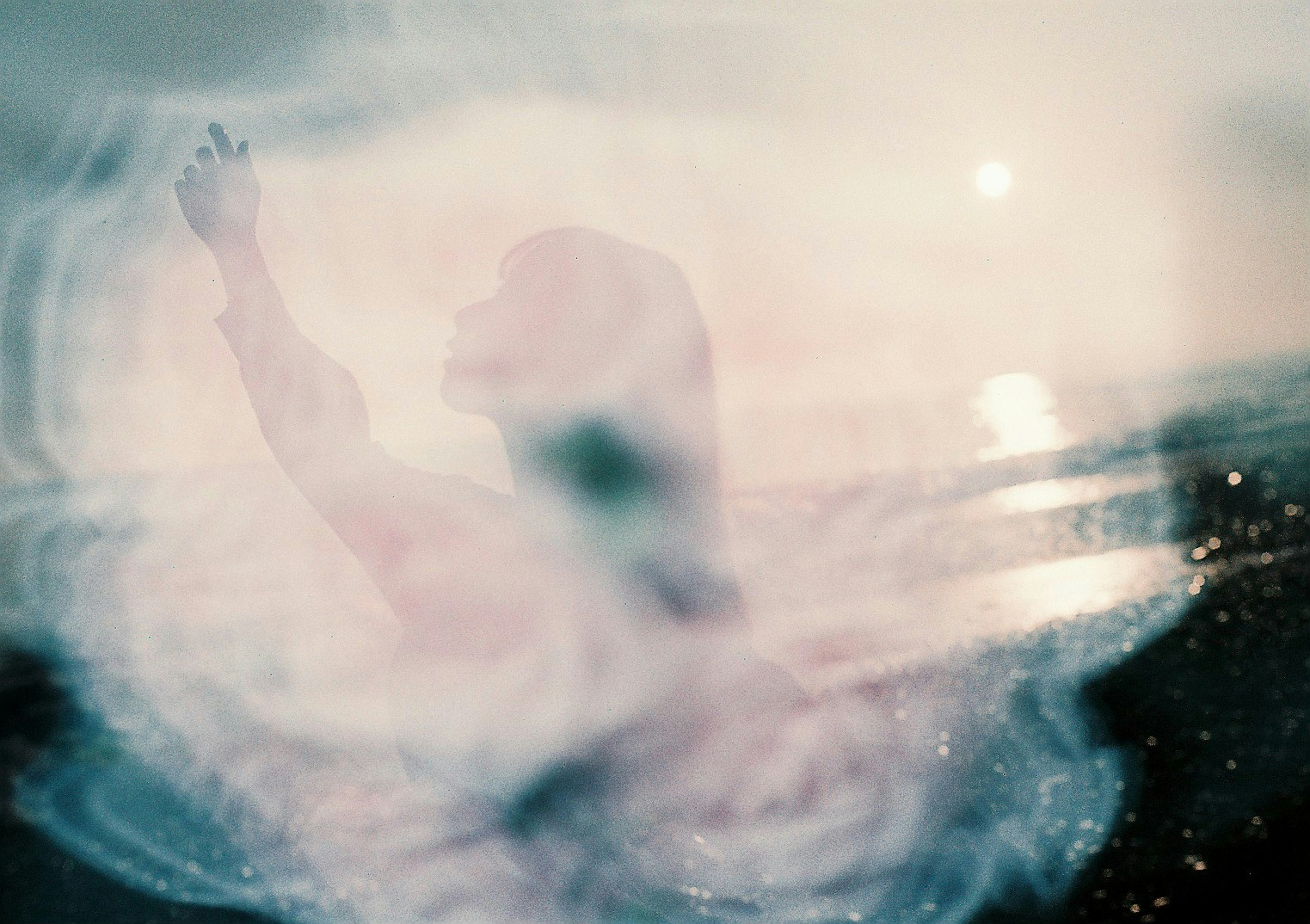 Abstract image featuring a silhouette of a person with raised hands against a beach and light reflections