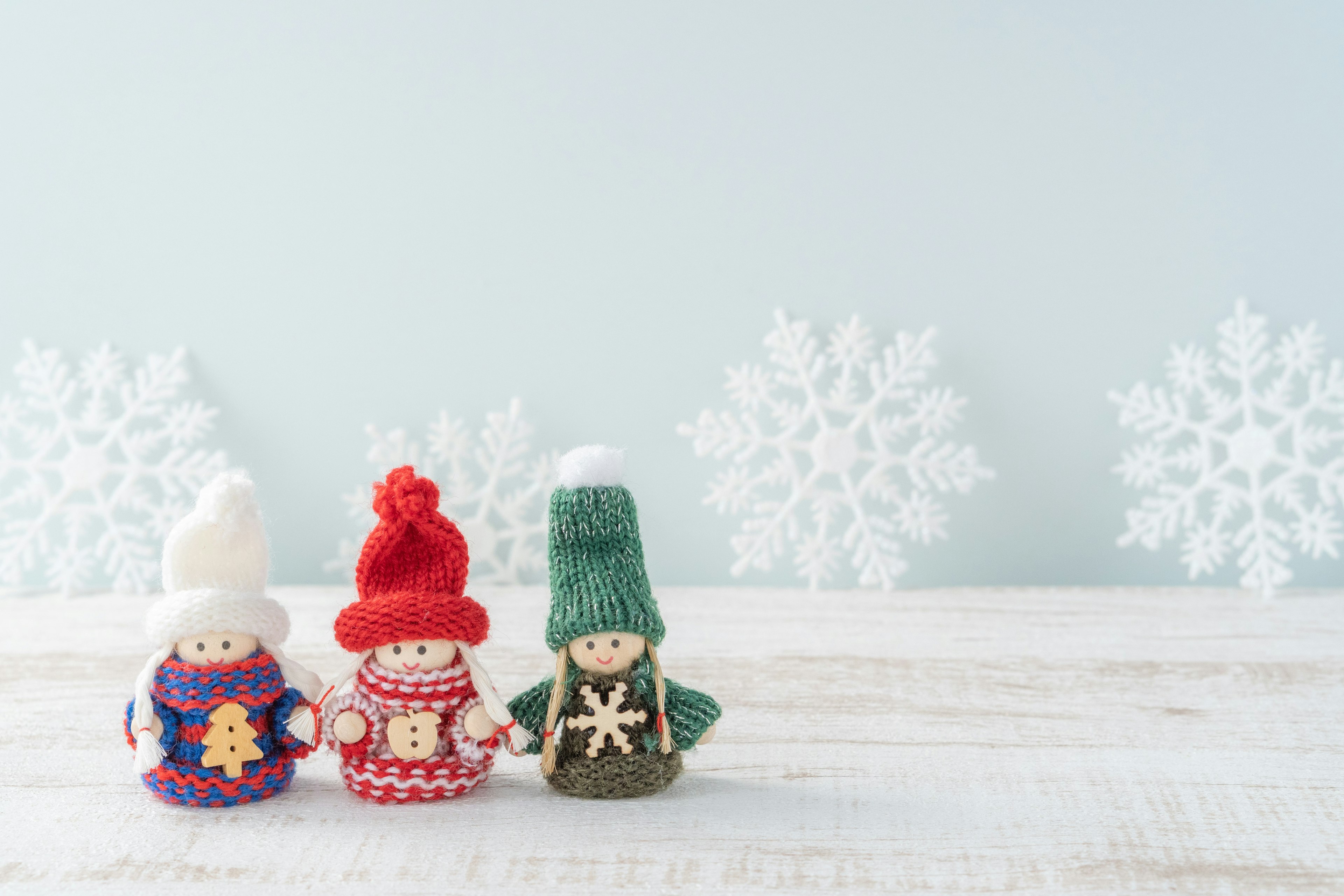 Tres muñecos de lana con gorros de invierno contra un fondo de copos de nieve