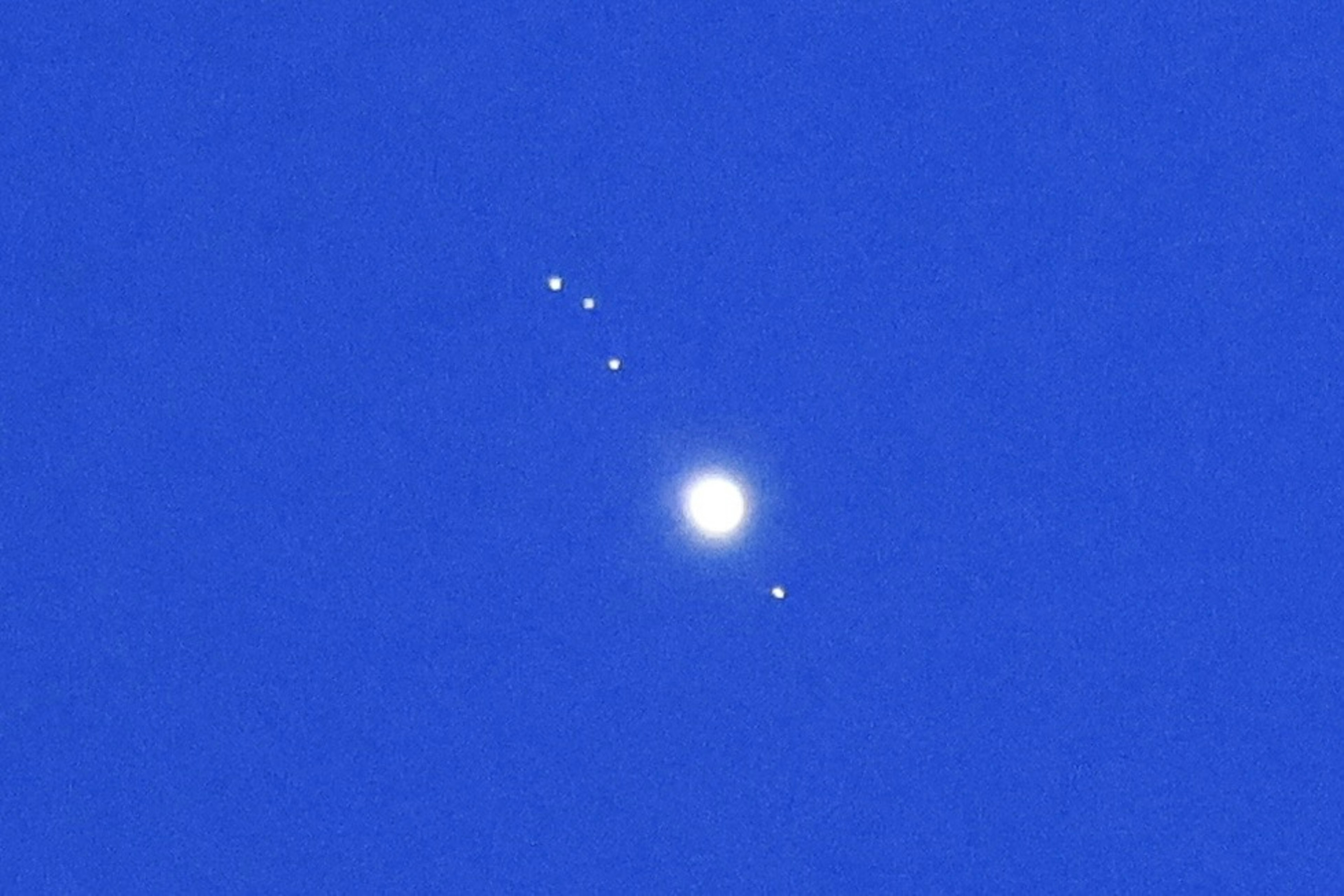 青い空に浮かぶ明るい木星とその周りの衛星