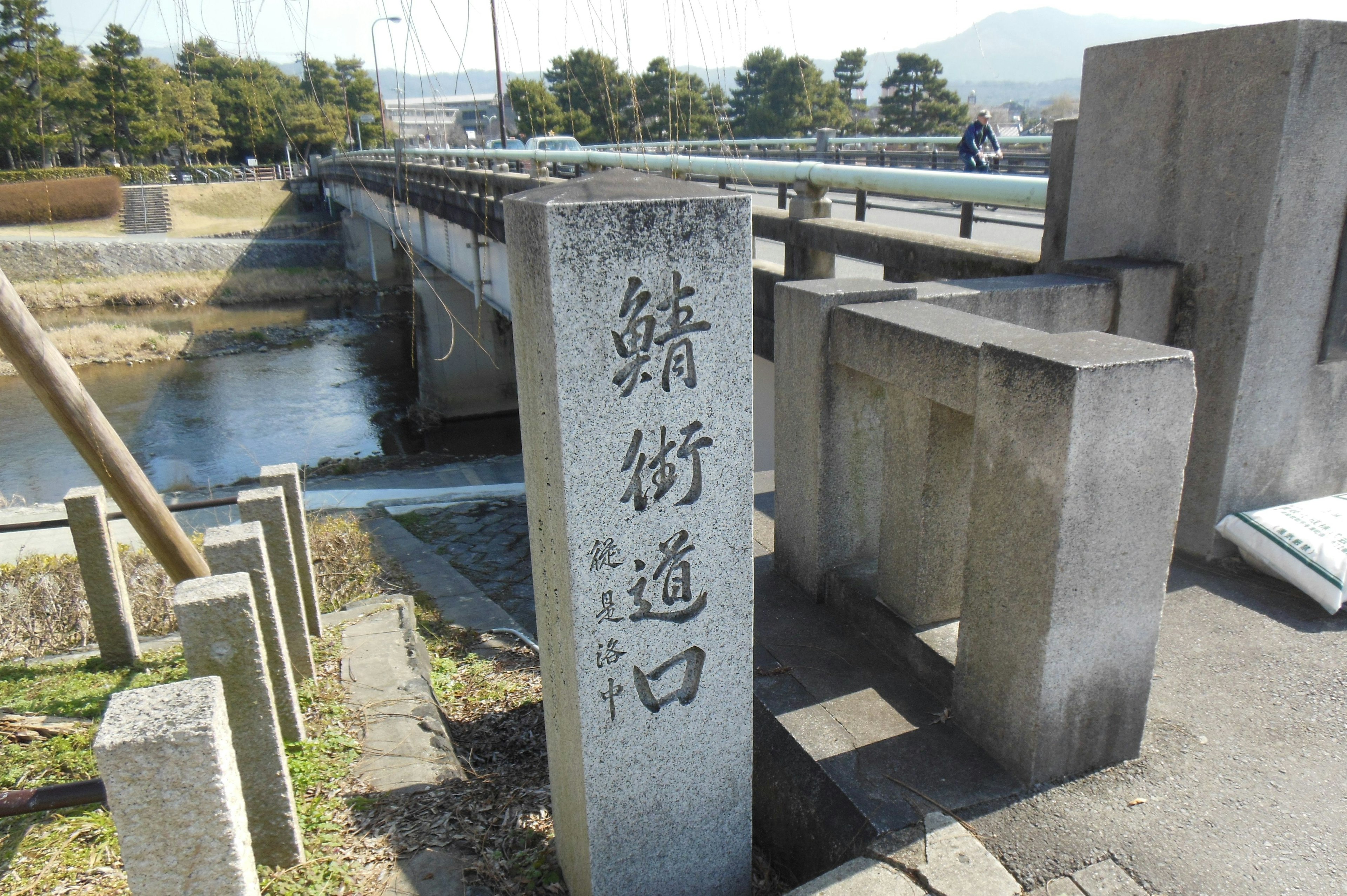 Steinschild in der Nähe einer Brücke mit Inschriften und umliegender Landschaft