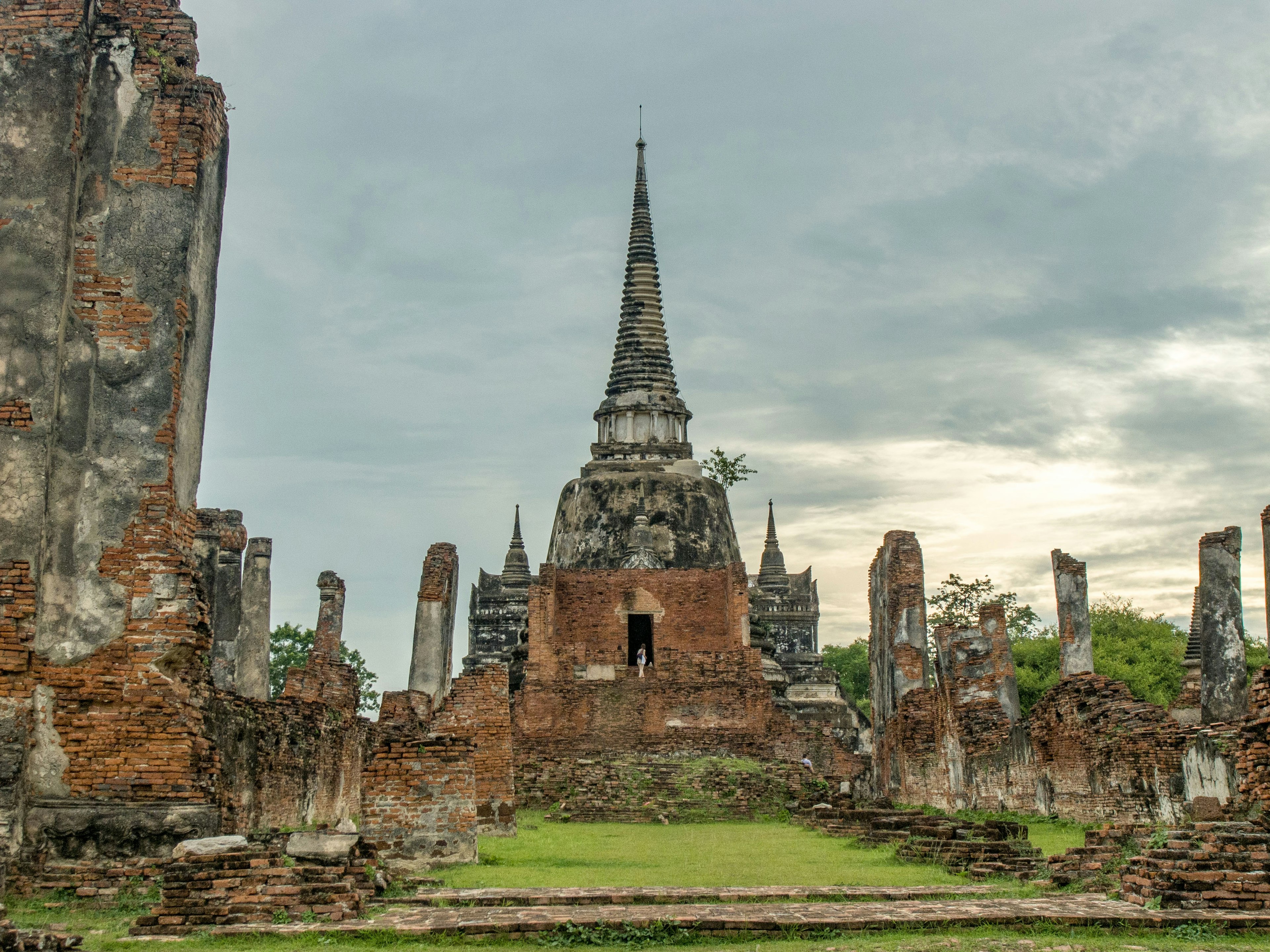 Ruinen des historischen Tempelkomplexes von Ayutthaya mit einem hohen Turm im Hintergrund