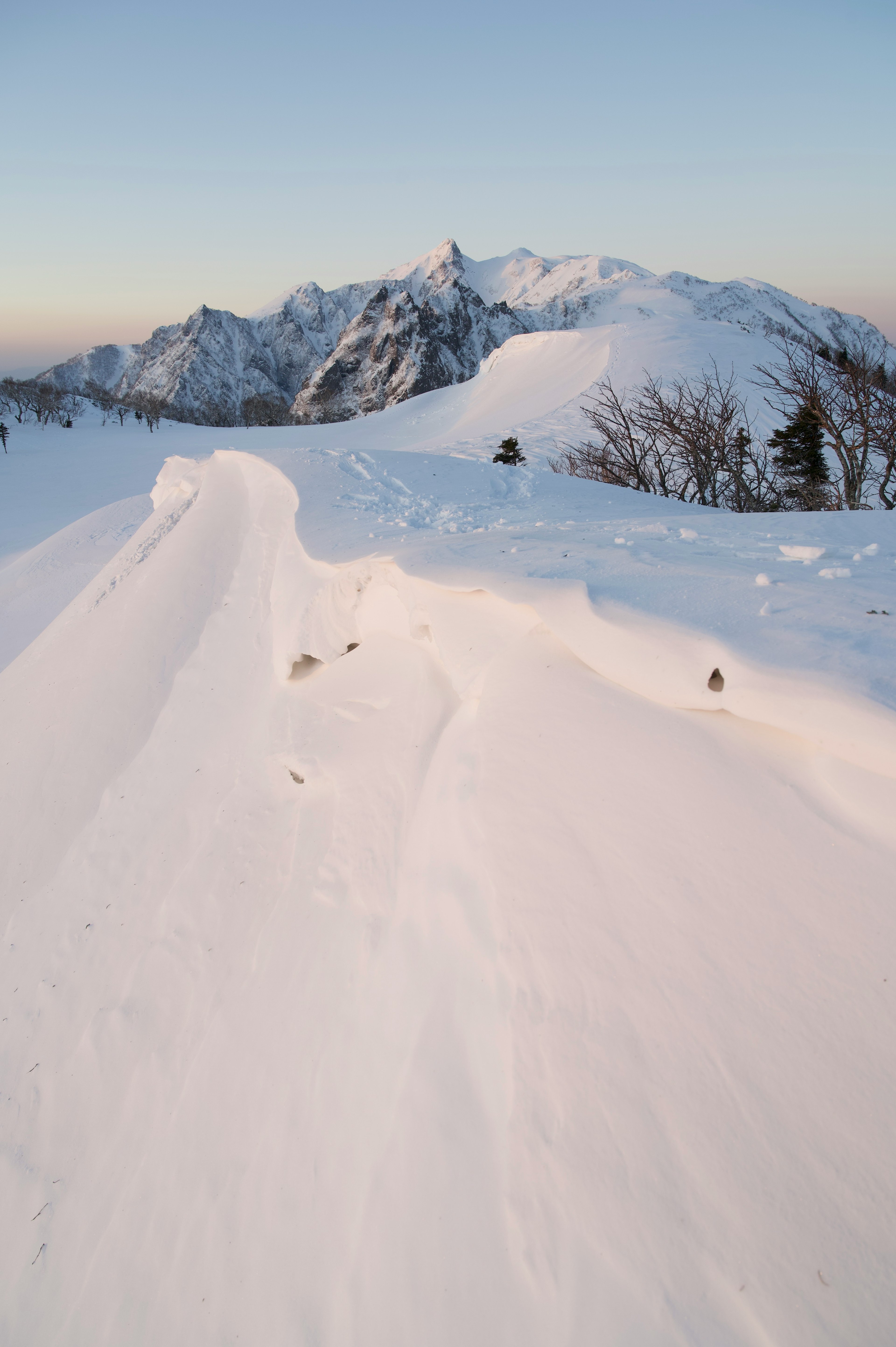 Paisaje montañoso cubierto de nieve con ventiscas y picos escarpados al fondo