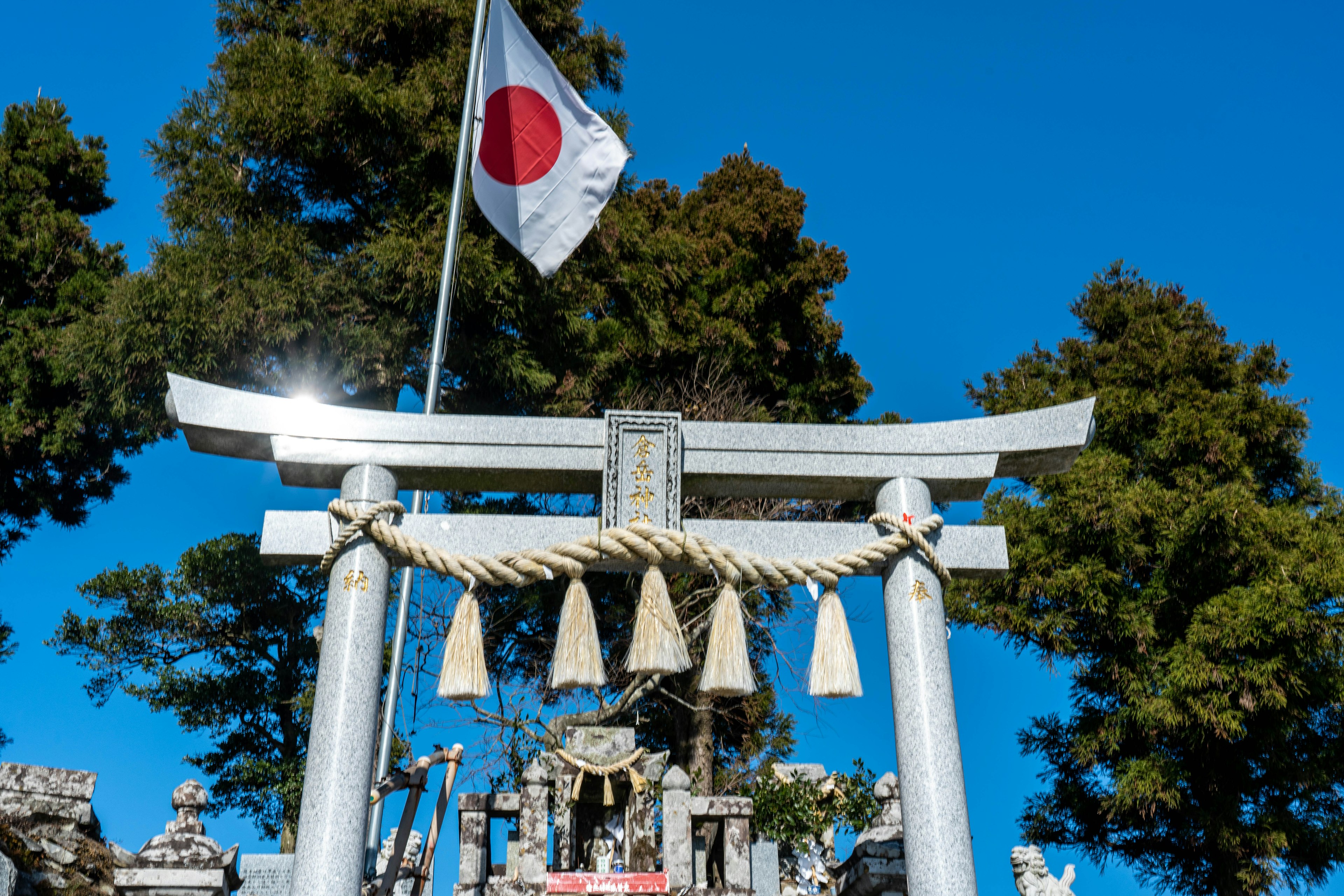 Cổng torii của đền thờ Nhật Bản dưới bầu trời xanh với cờ Nhật Bản