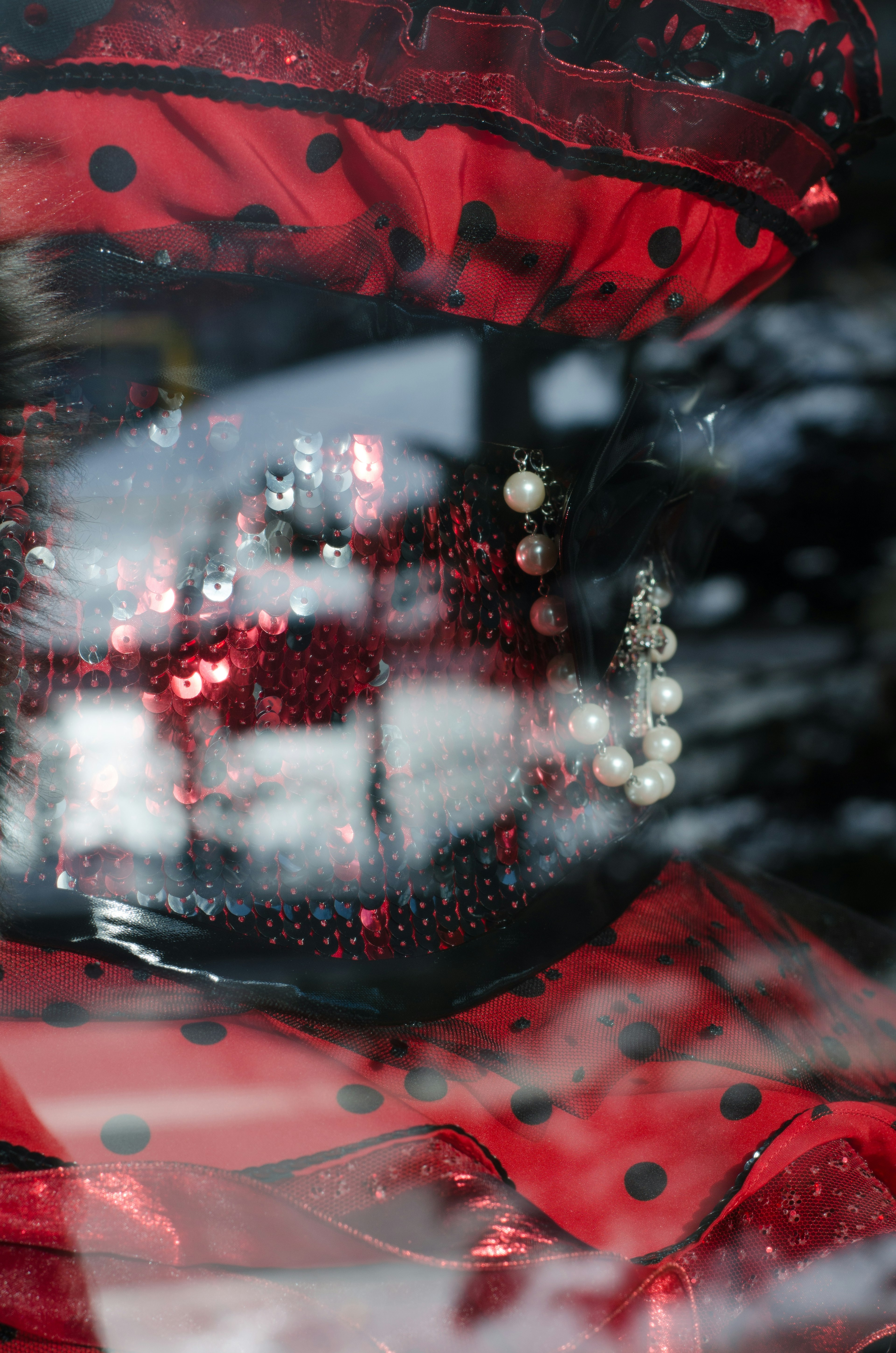 A red and black dress with a pearl necklace reflected through glass