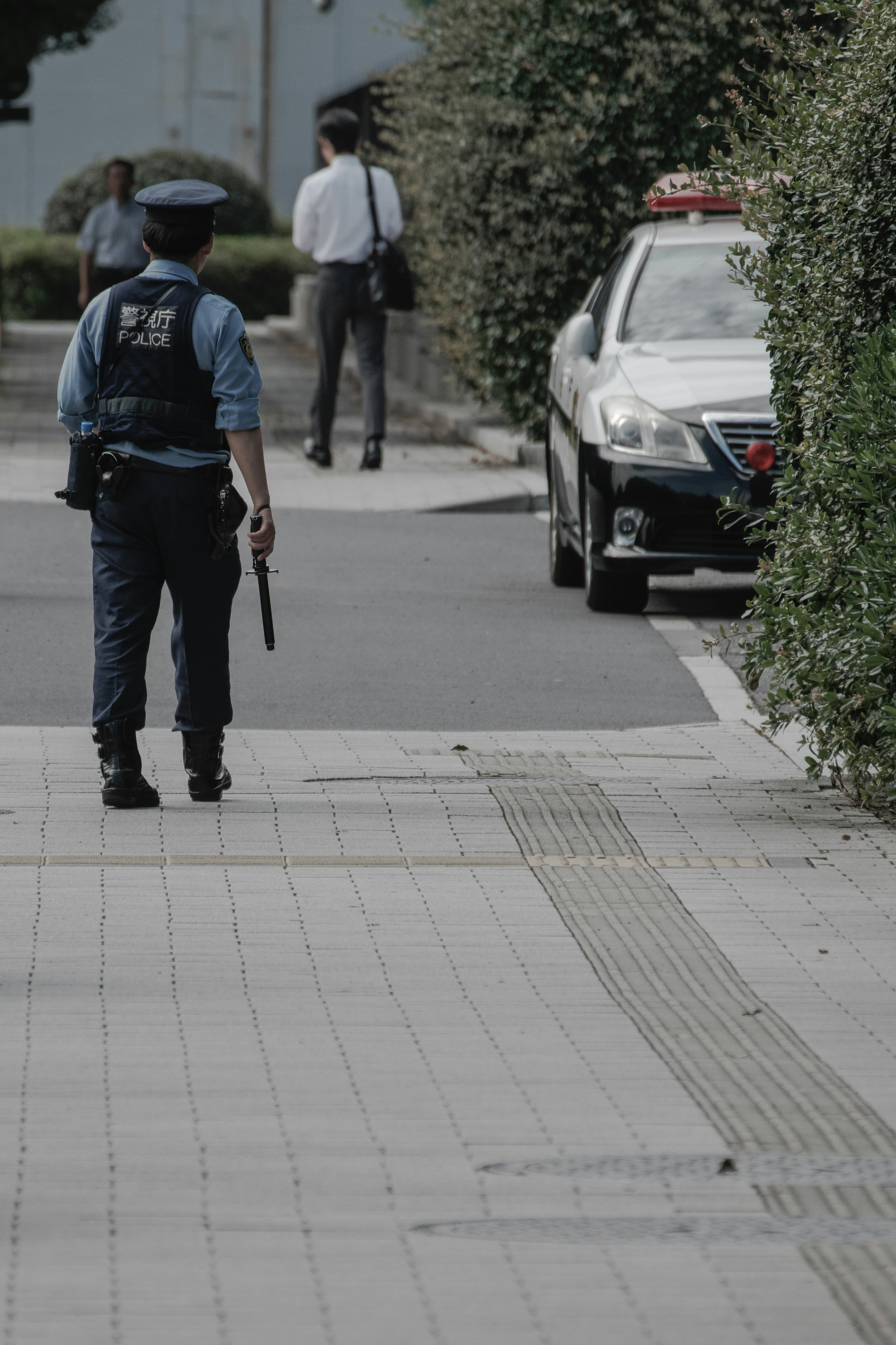 Un poliziotto che cammina sul marciapiede in un contesto urbano con un'auto della polizia parcheggiata