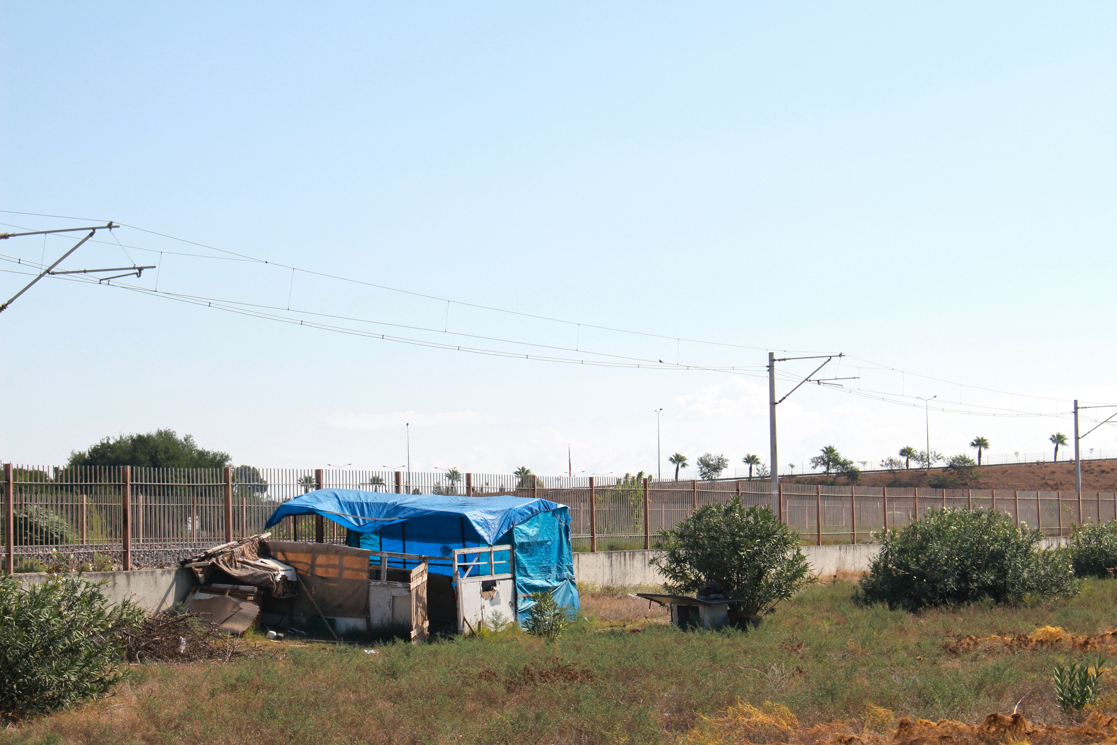 Ein provisorisches Shelter mit blauer Plane umgeben von Gras und Bahngleisen