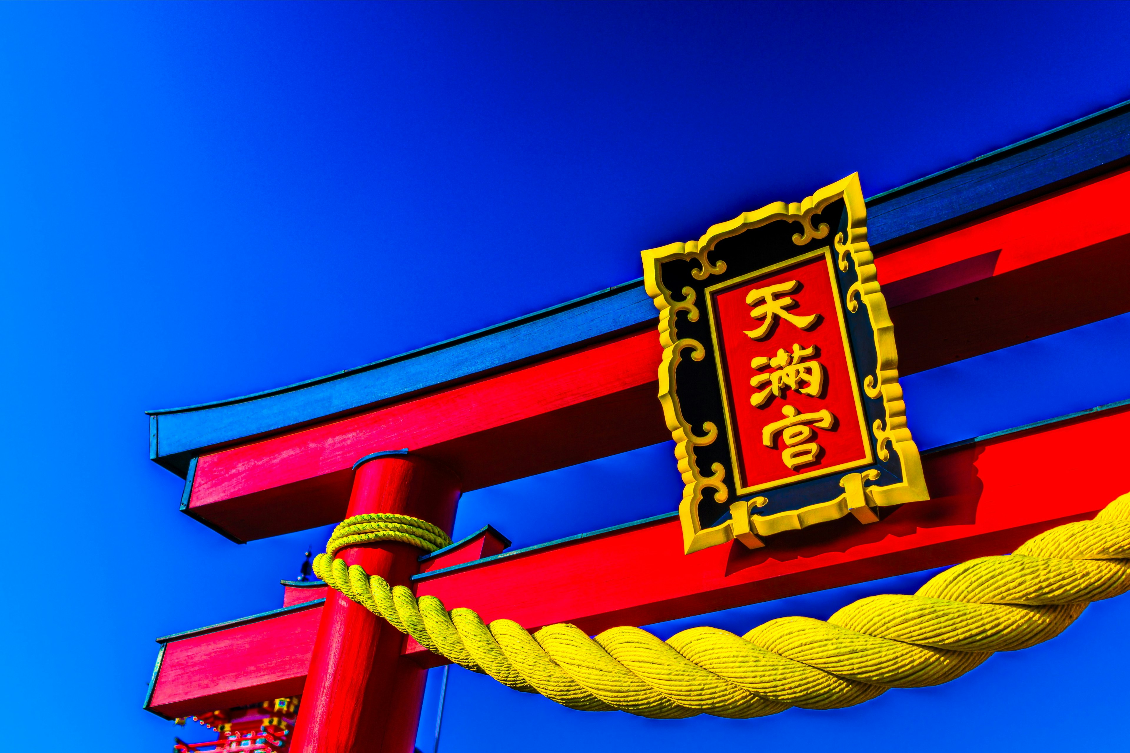 Torii gate of Tenmangu Shrine featuring red structure and yellow rope