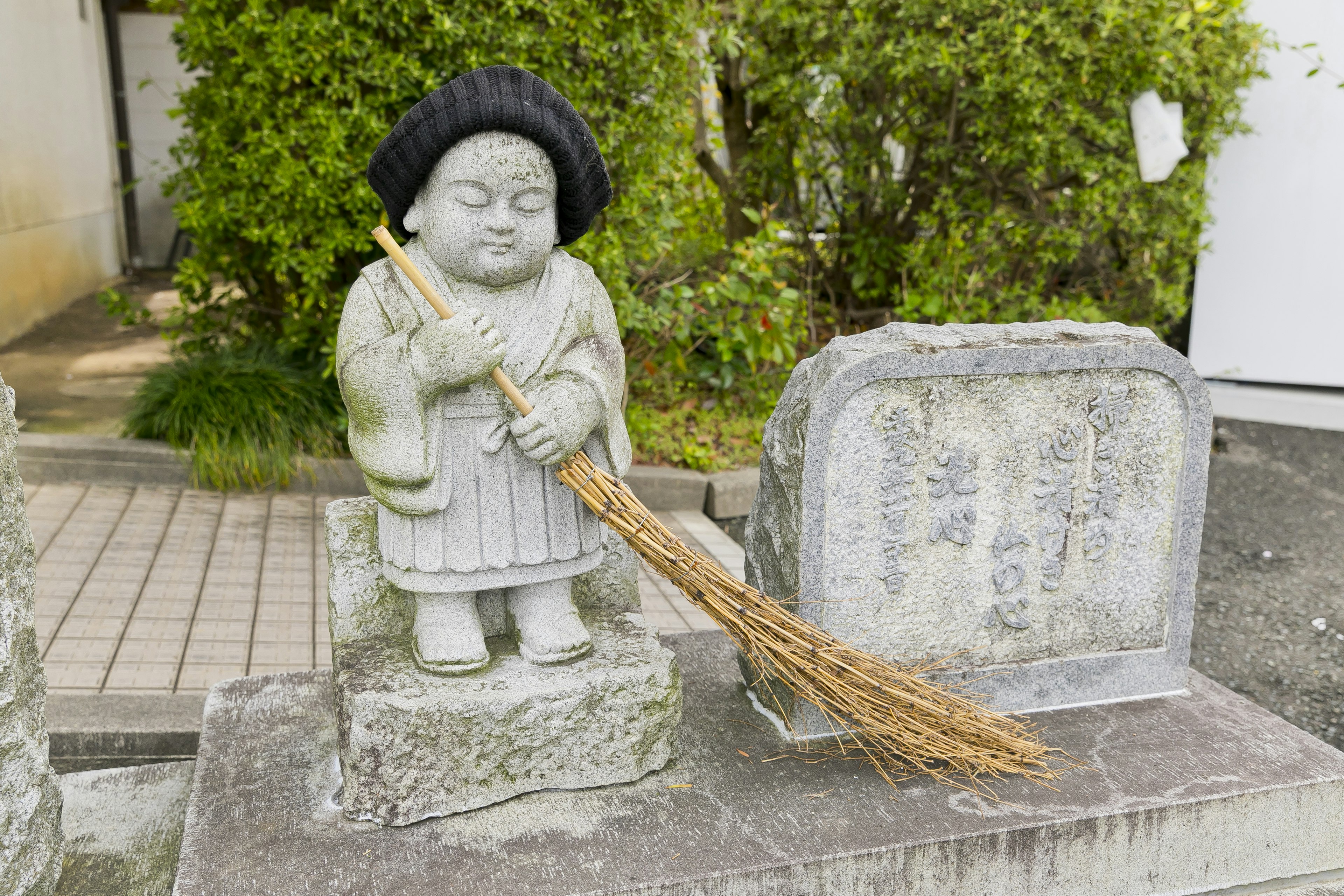 Steinstatue mit einem Besen in traditioneller Kleidung