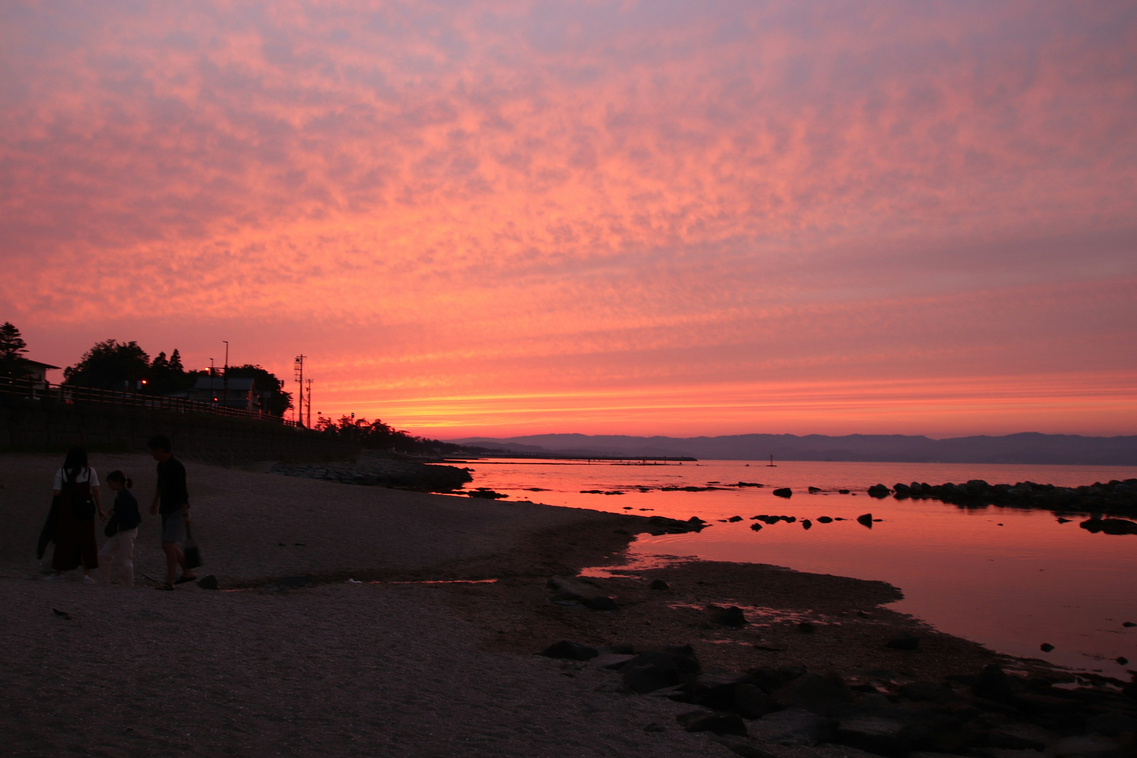 Personas caminando por una playa al atardecer con un hermoso cielo rosa