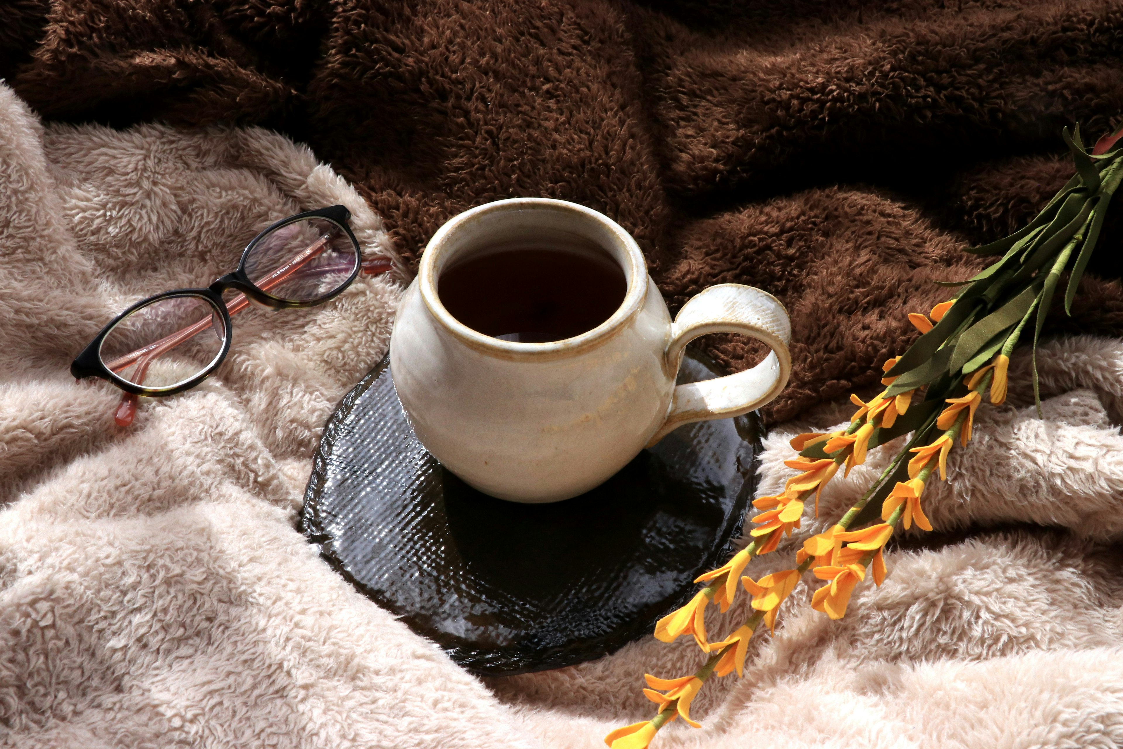 Una taza de cerámica blanca con una bebida caliente y flores naranjas sobre una manta suave