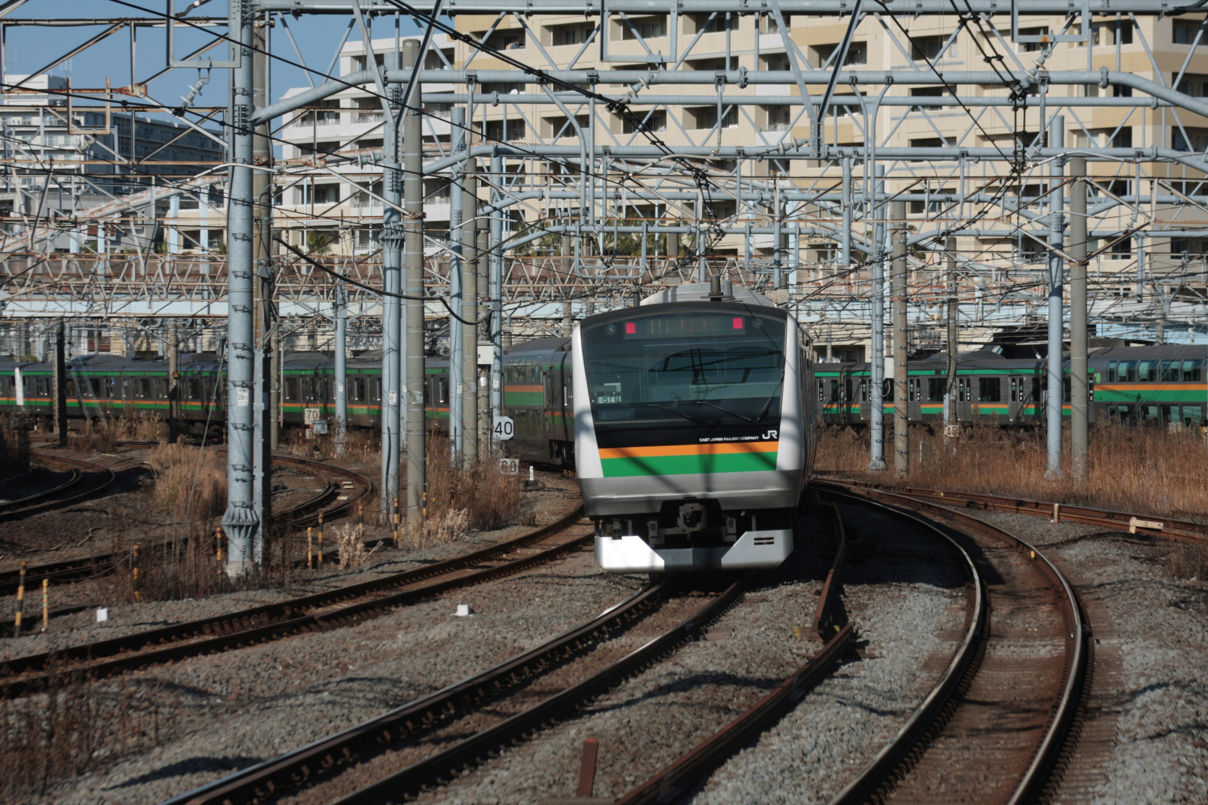 Japanische Bahnszene mit einem grün-weißen Zug, der auf ein gebogenes Gleis zufährt