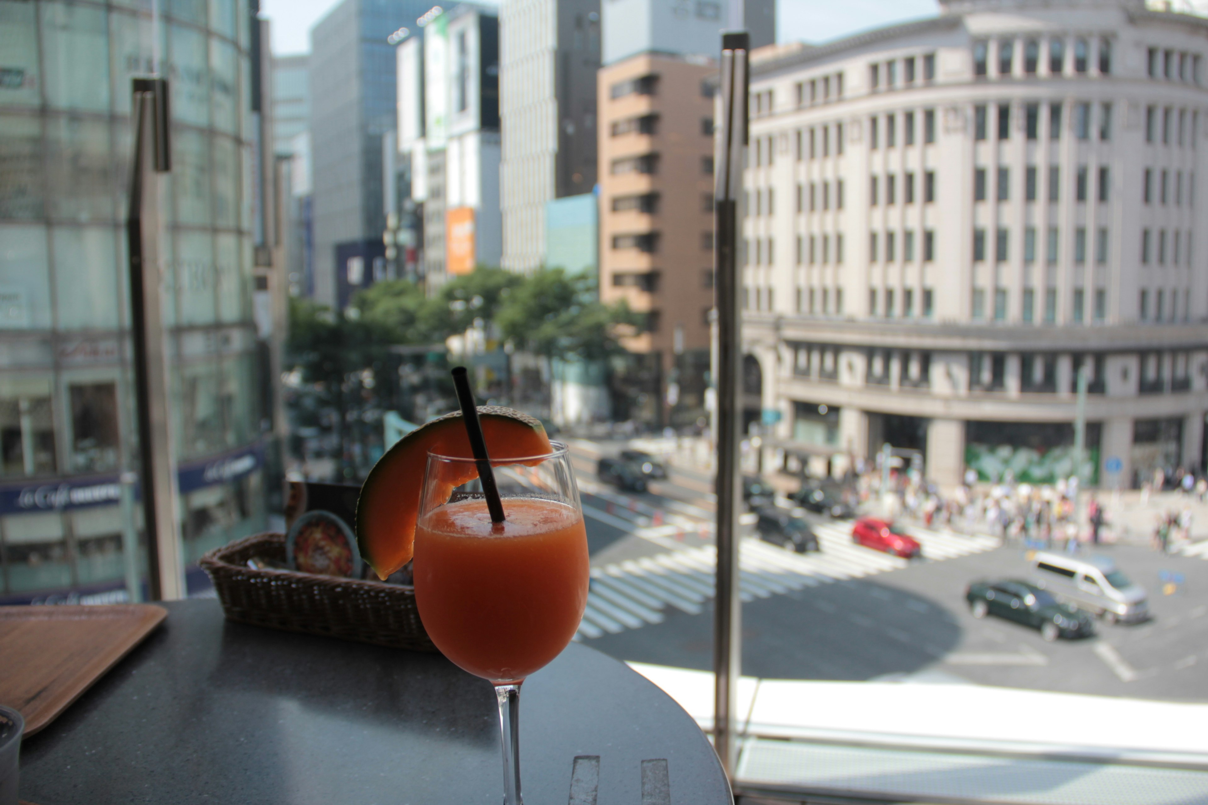 窓の外に都市の景色が広がるカフェのテーブルに置かれたオレンジ色のドリンク