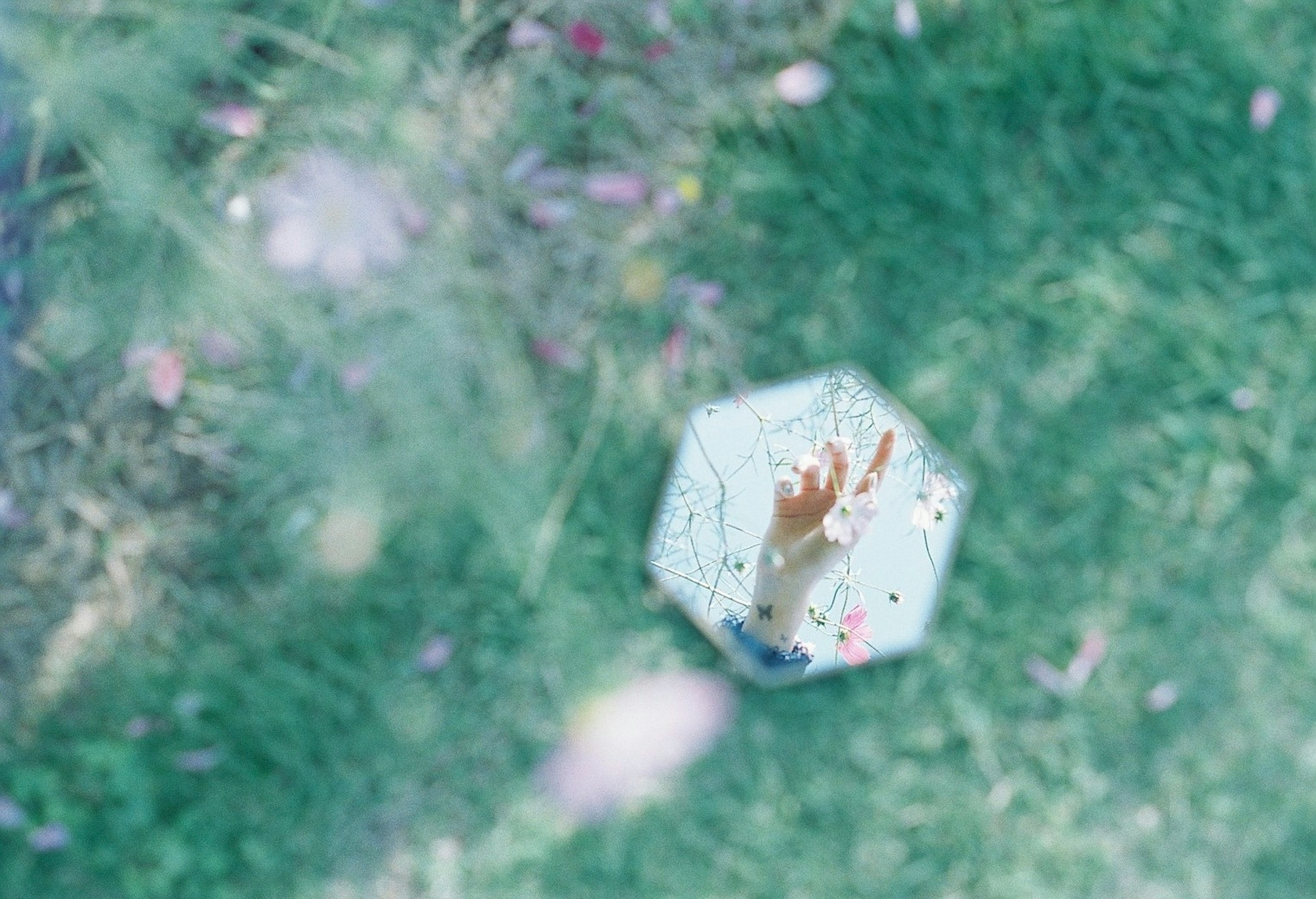 Main reflétée dans un miroir hexagonal sur l'herbe