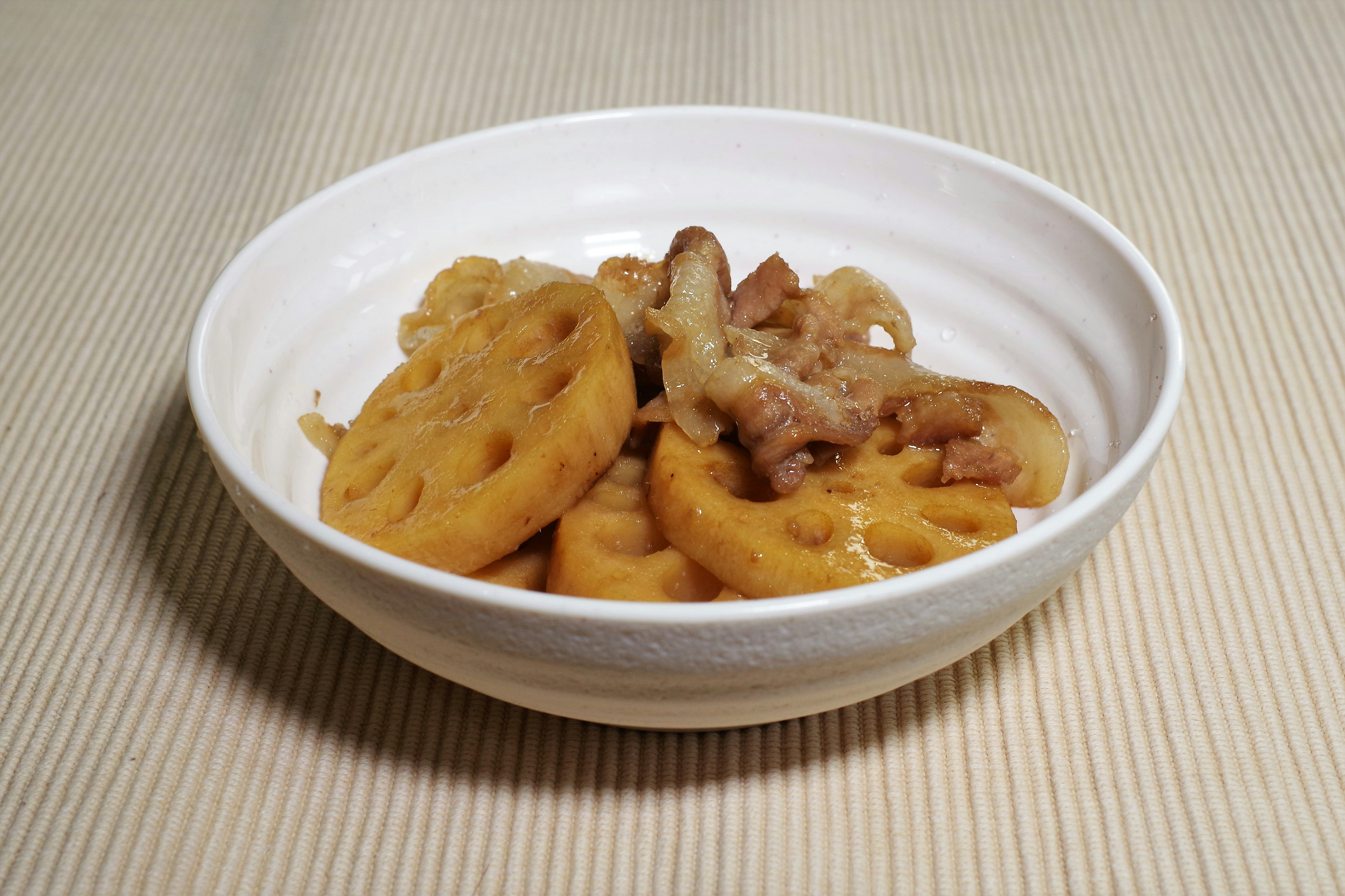 Plato de raíz de loto servido en un tazón blanco con carne y salsa dulce por encima