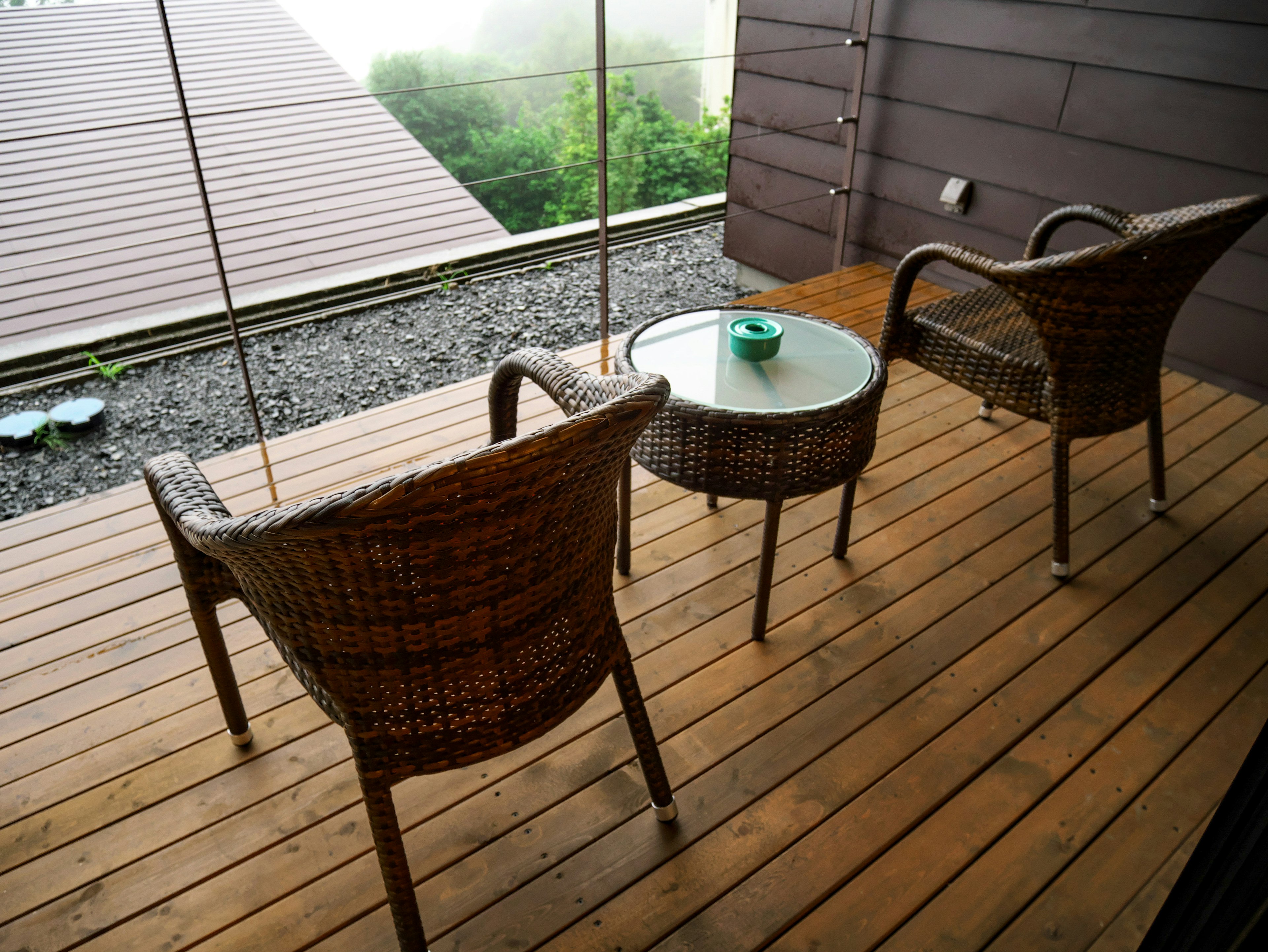 Two wicker chairs and a glass table on a wooden deck