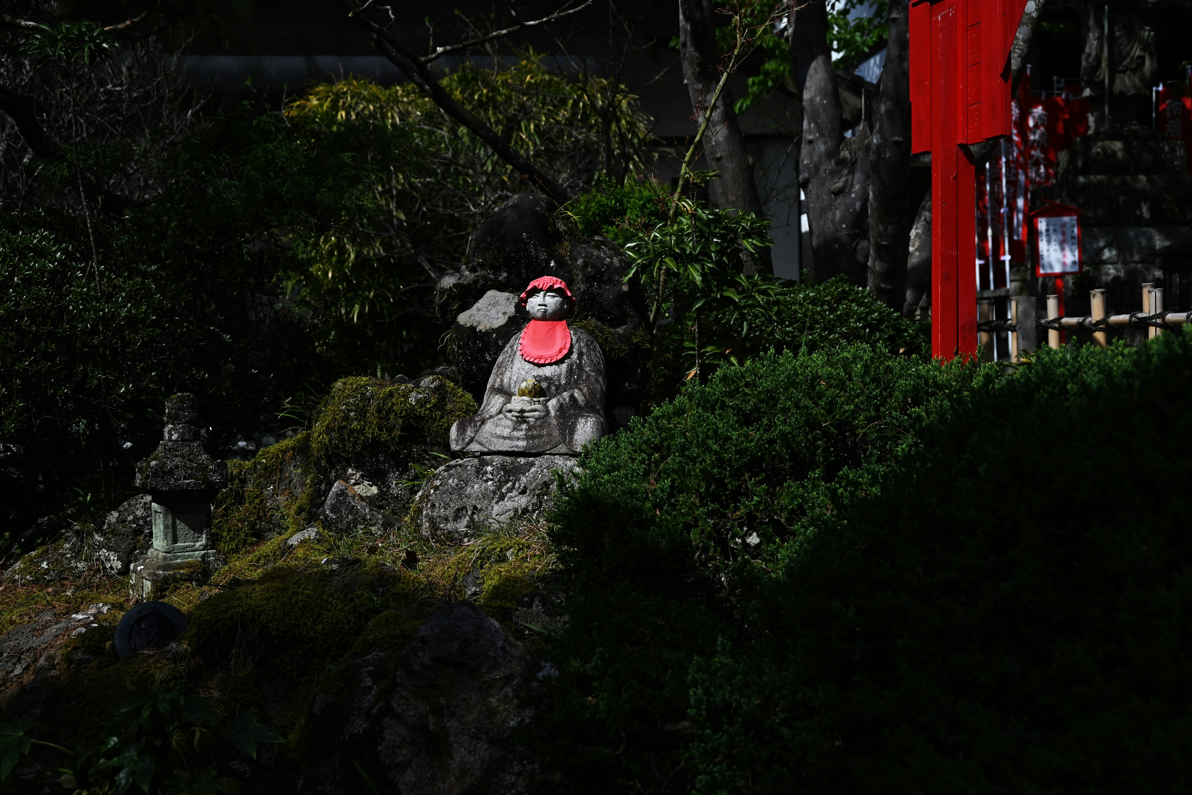 A stone statue wearing a red hat surrounded by green plants