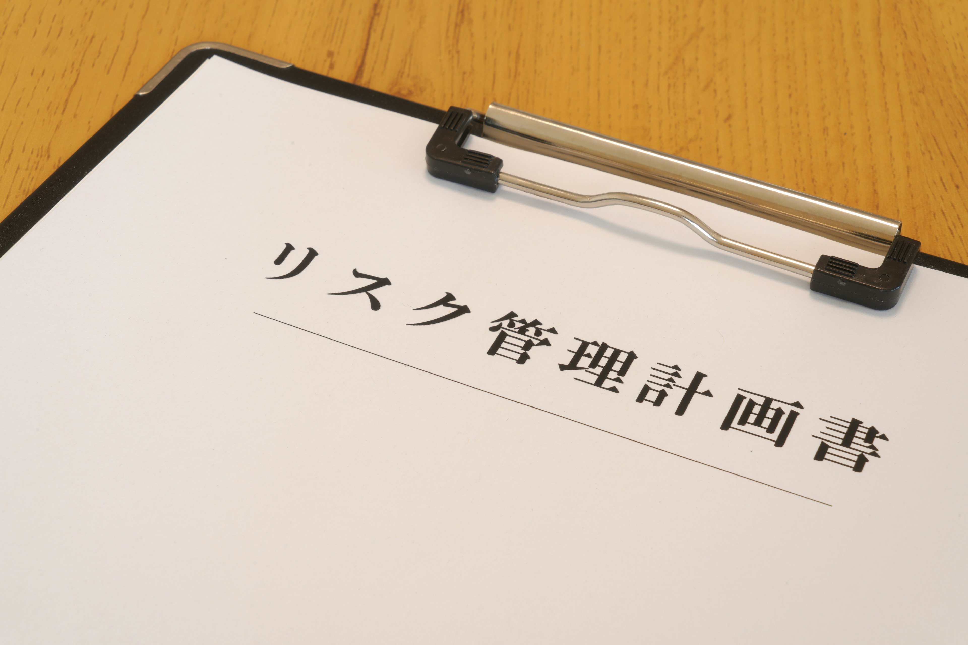 クリップボードに置かれた白い紙に書かれたリスク管理計画書のタイトル