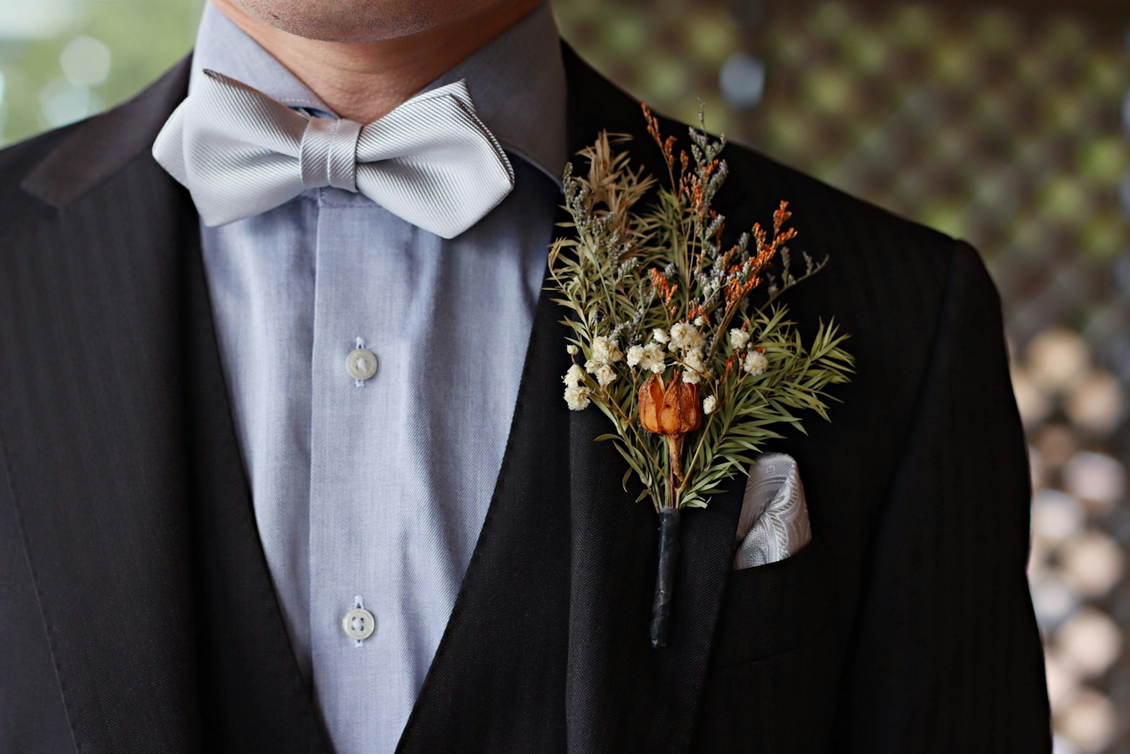 A close-up of a man's tuxedo featuring a boutonnière with orange flowers and green foliage