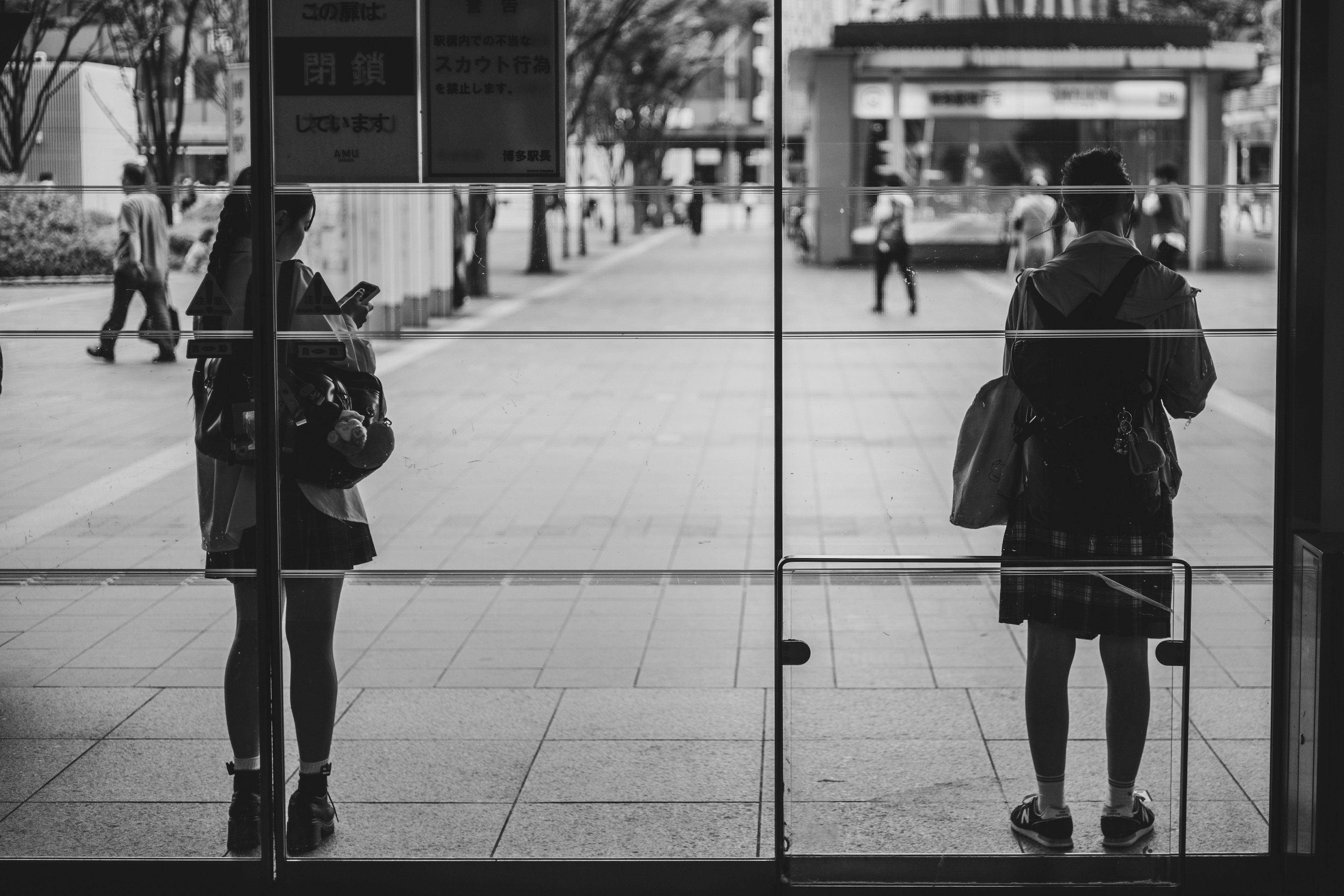 Two women standing behind glass doors with people walking outside