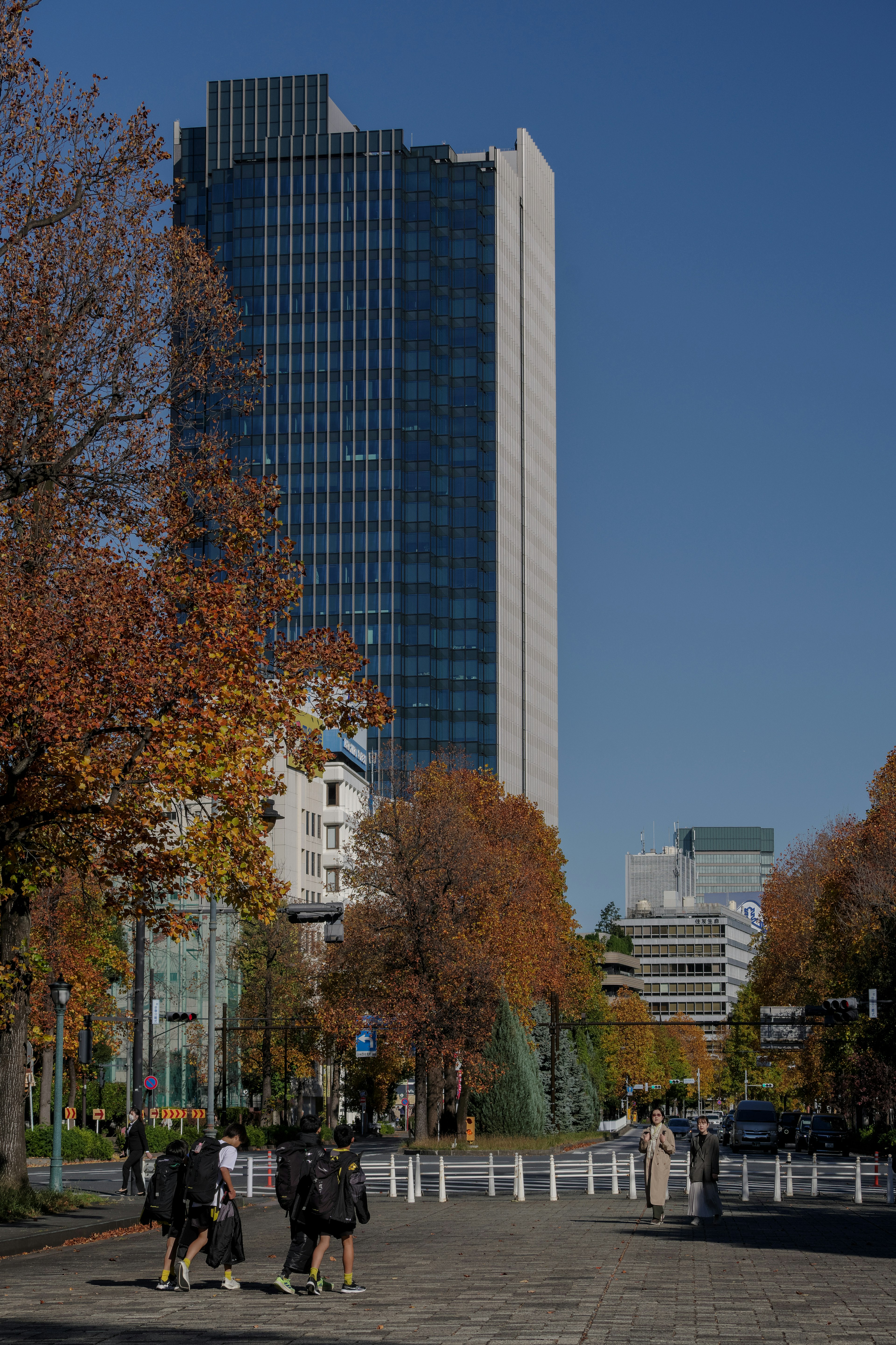 Hochhaus mit herbstlichem Laub und Fußgängern