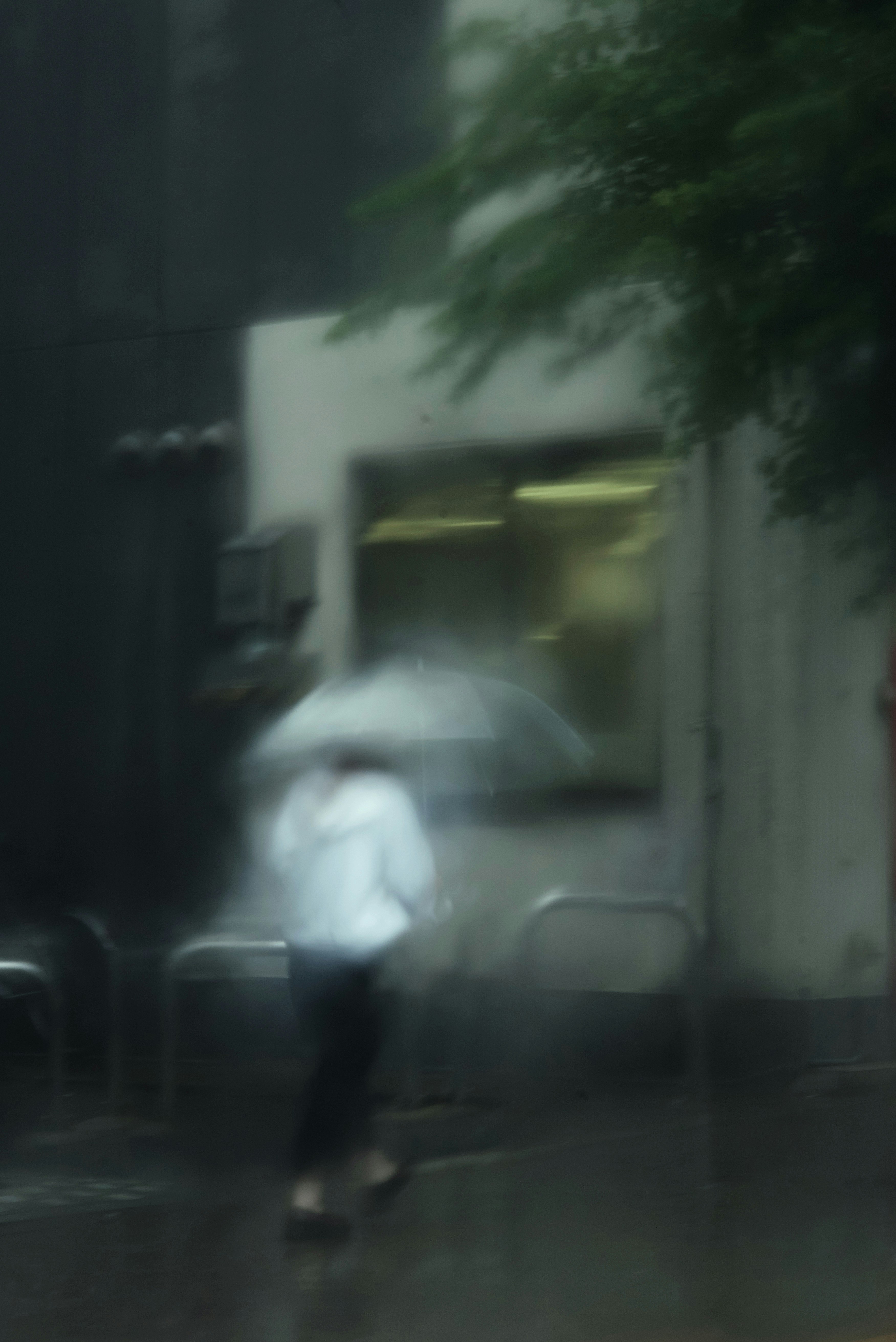 穿着白色衣服的人在雨中走着,手持雨伞,背景模糊的建筑