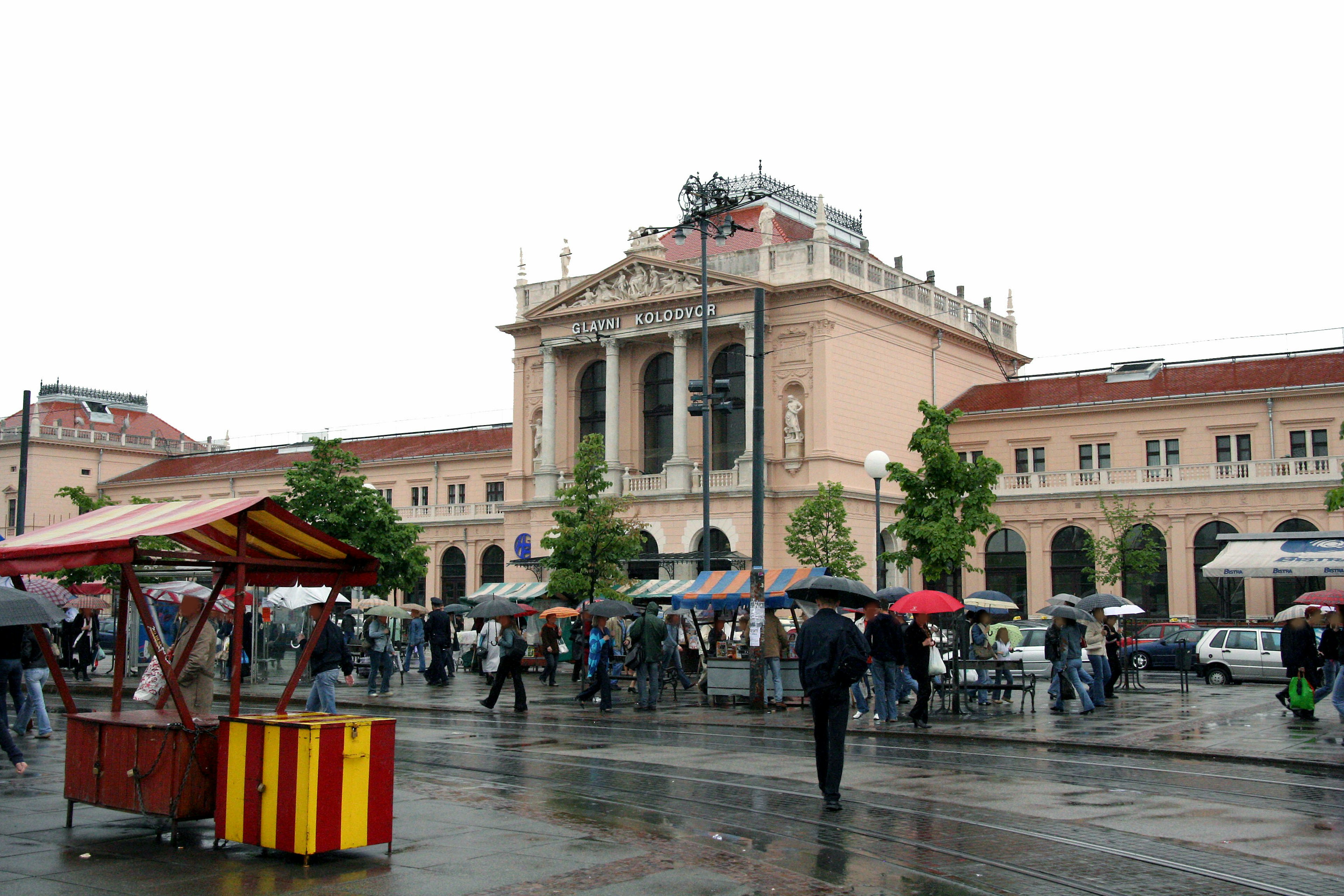 Historic train station building in a rainy square with market stalls