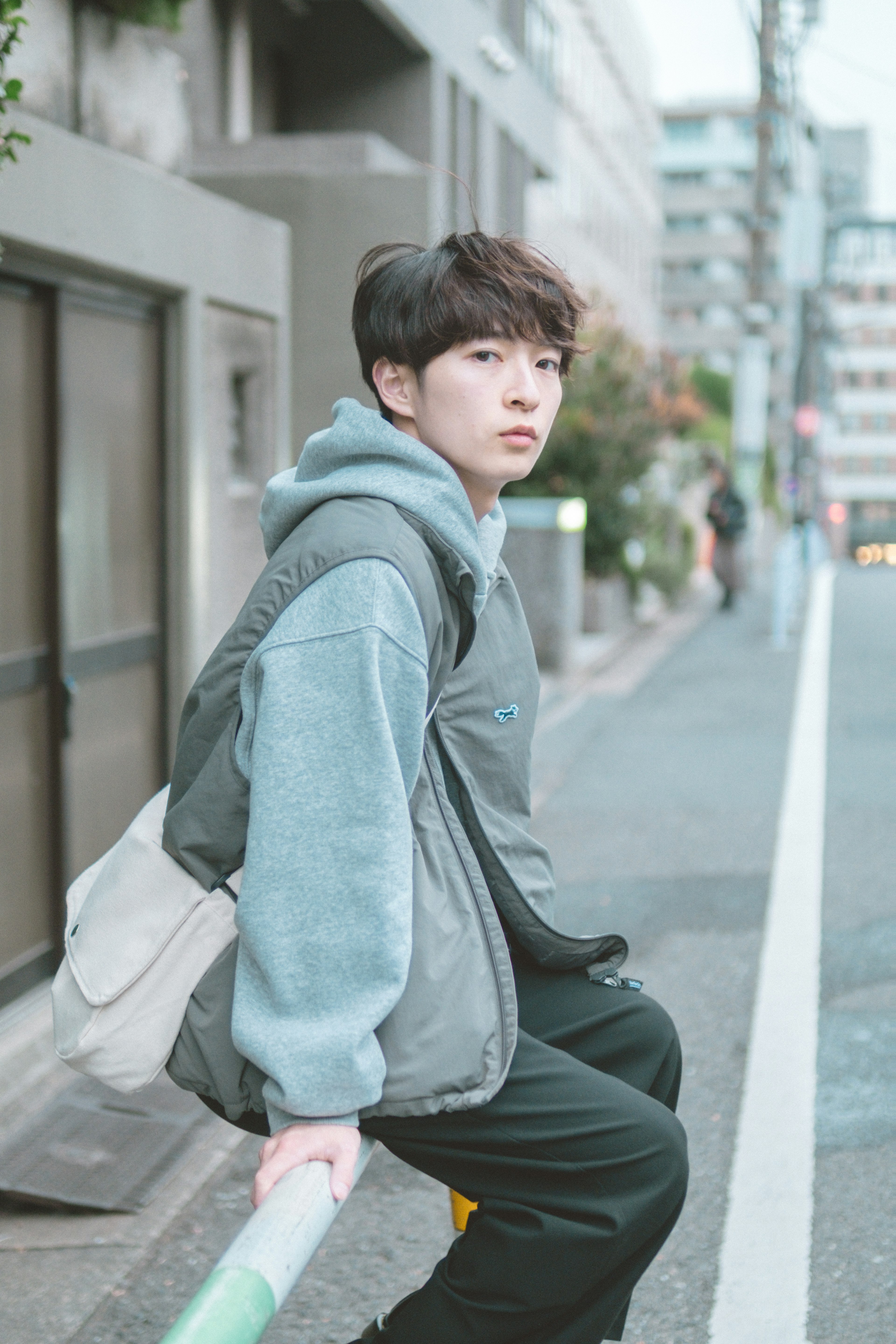 A young person sitting on a street bench wearing casual fashion and a thoughtful expression