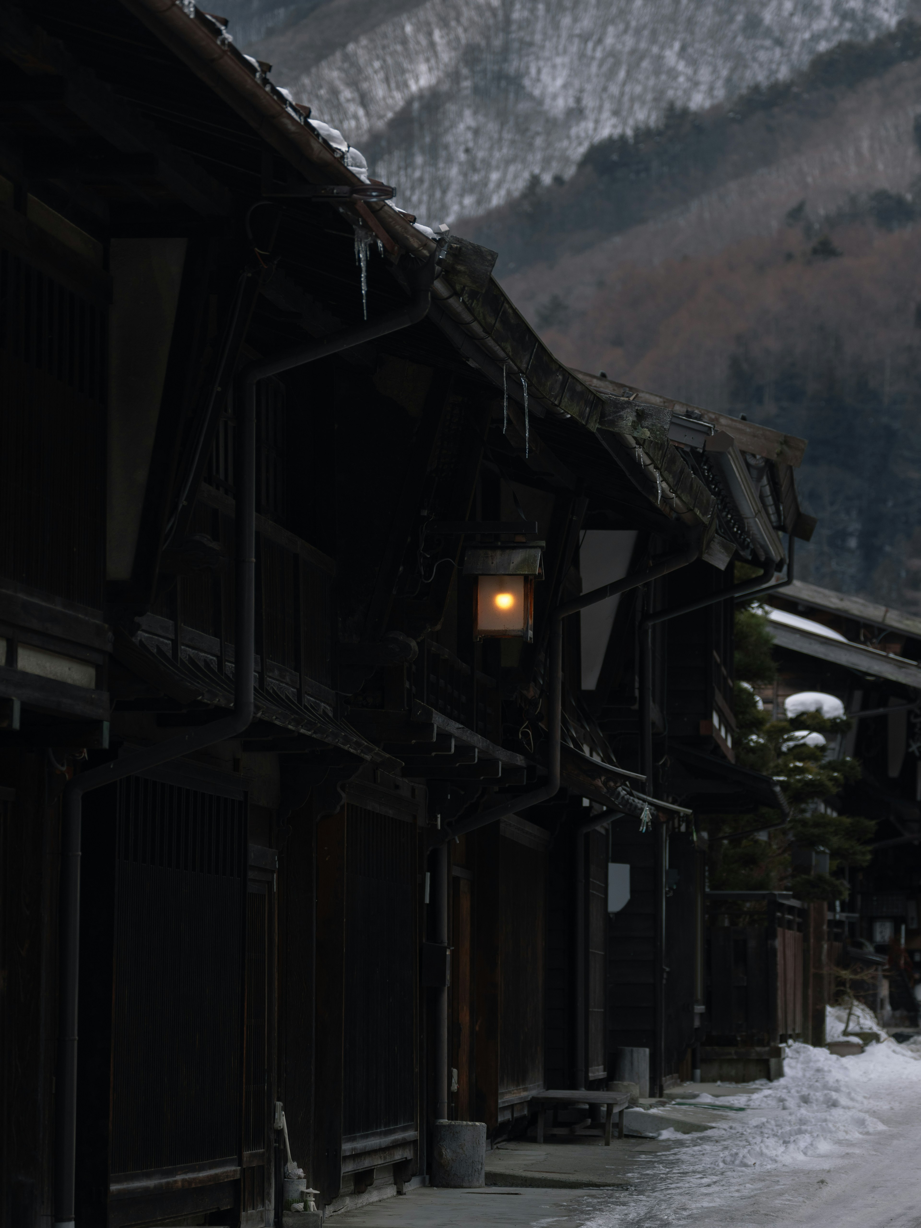 雪に覆われた山の背景の古い木造家屋と暖かい光のランプ