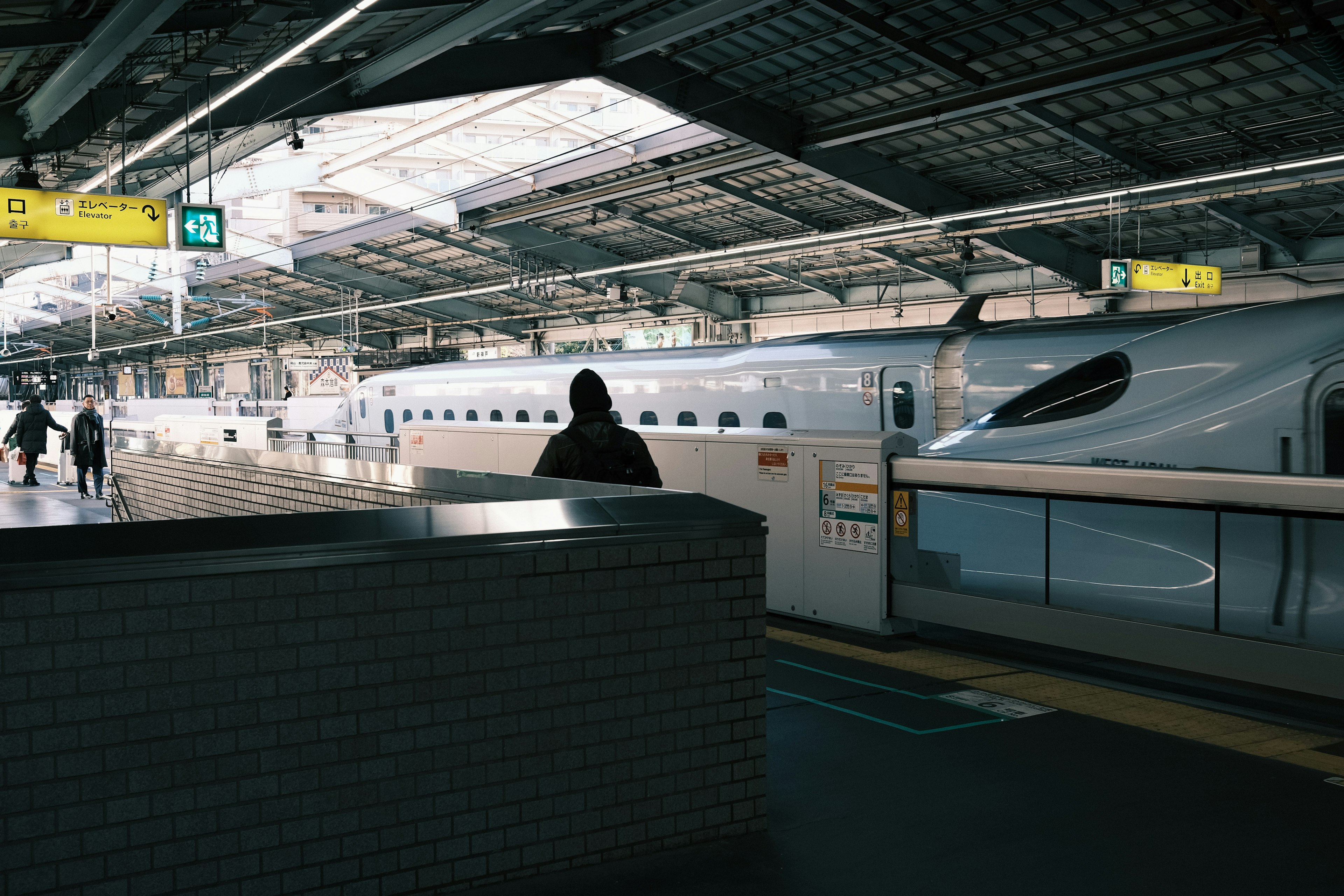 Innenansicht eines Bahnhofs mit einem geparkten Shinkansen Menschen, die sich in der Nähe eines Schalts stehen