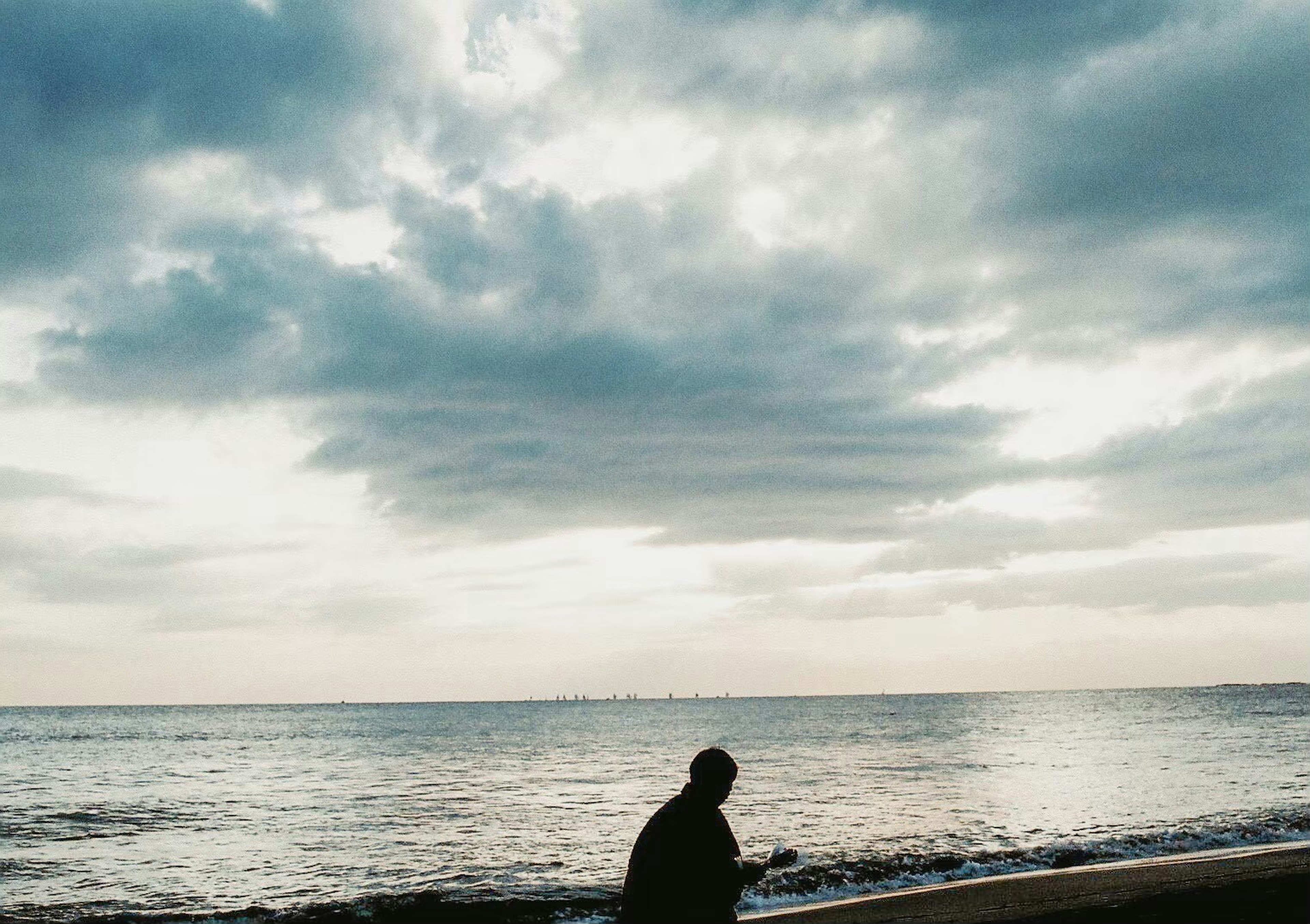 Silhouette einer Person, die ruhig am Meer steht unter einem bewölkten Himmel