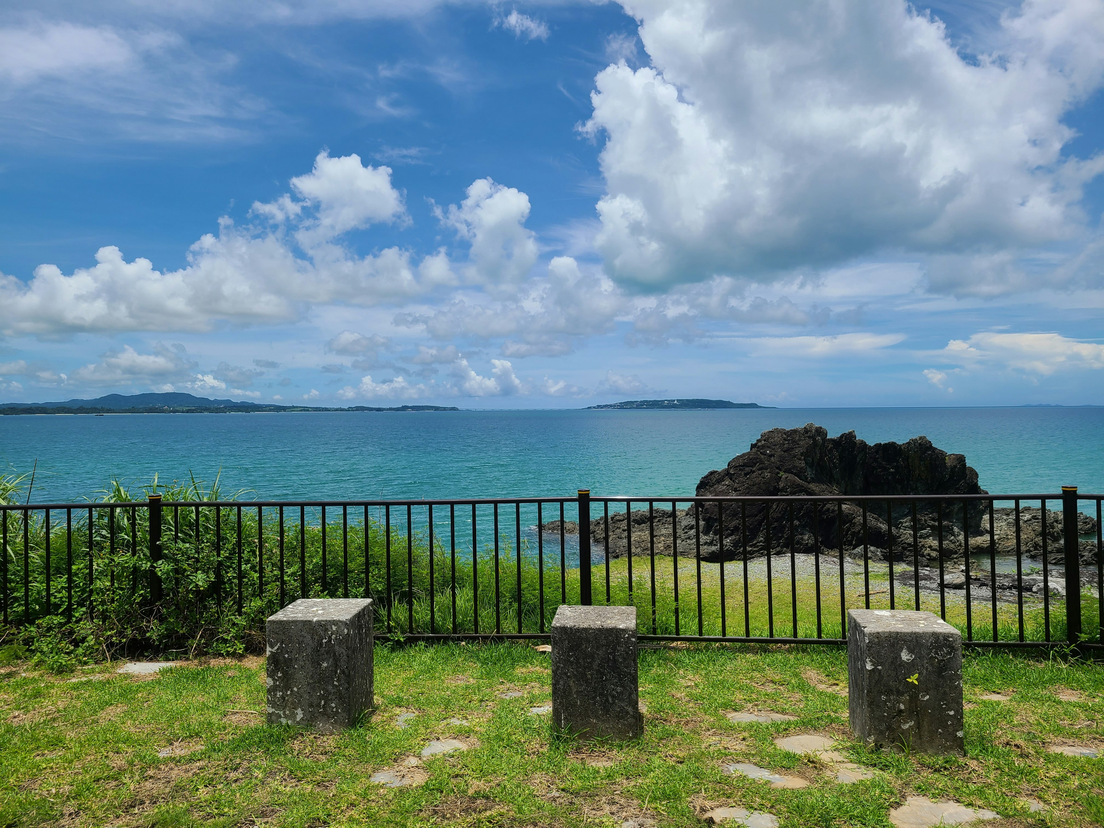 青い海と白い雲が広がる風景に石のベンチが並ぶ景色