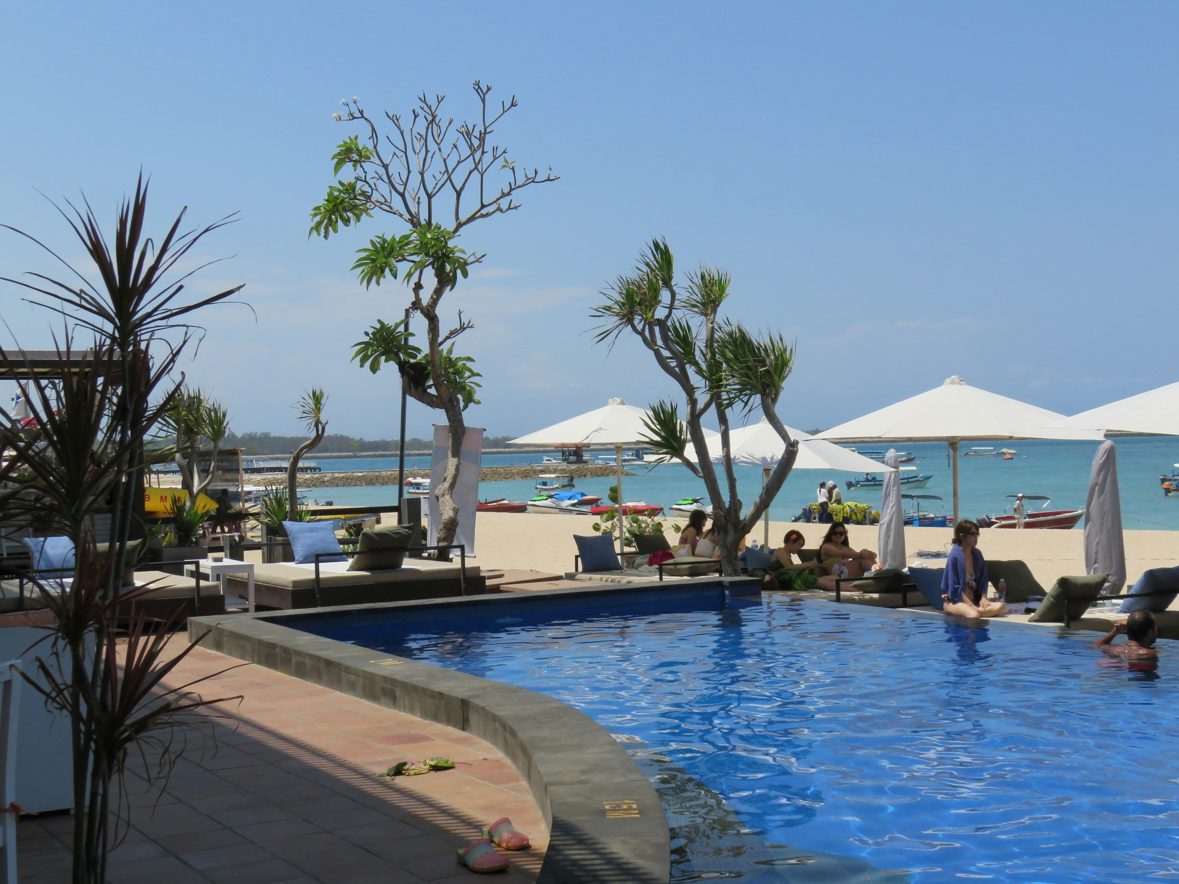 Vista di un resort sulla spiaggia con piscina blu e ombrelloni bianchi