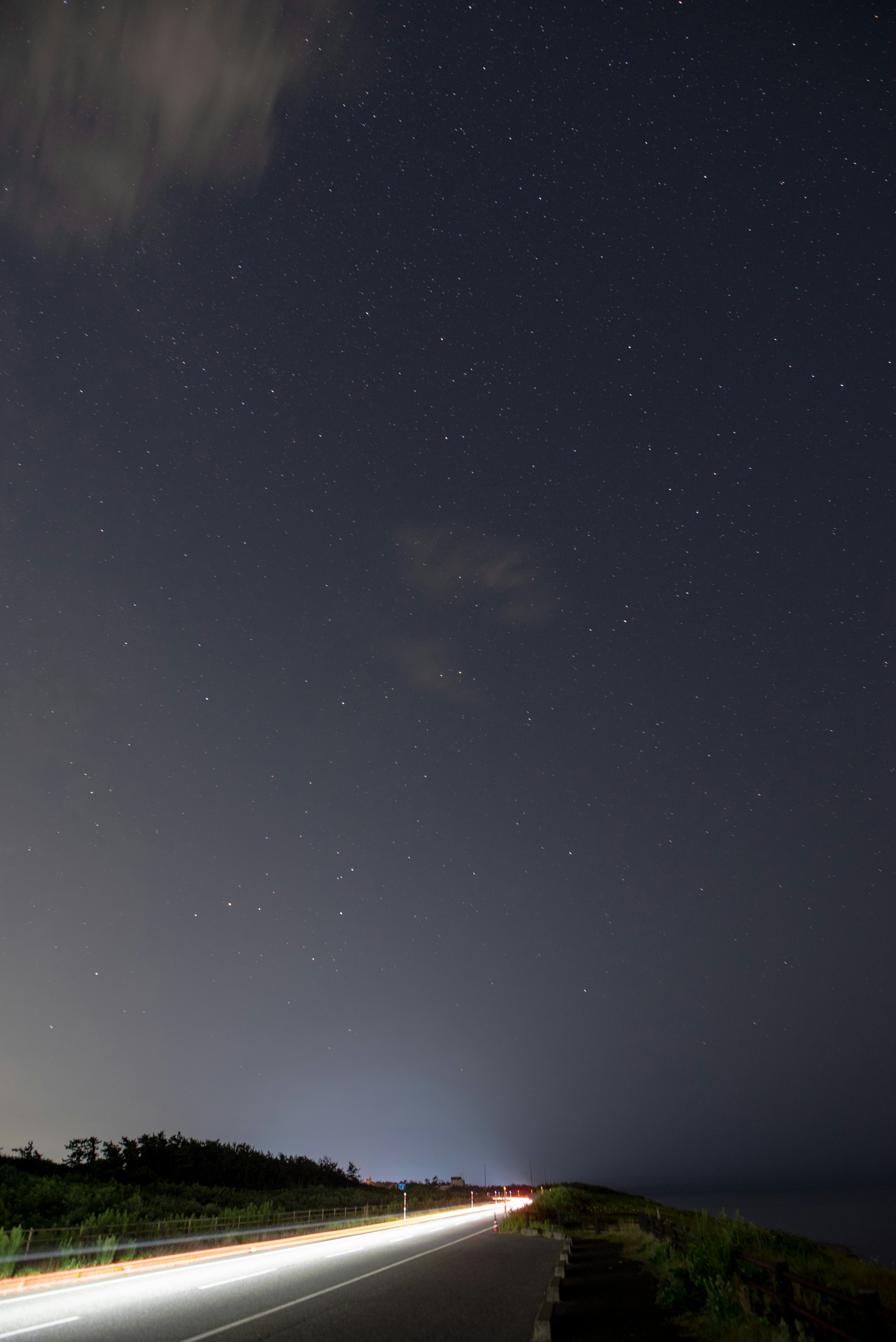 Straße unter einem sternenklaren Himmel mit Lichtspuren von Fahrzeugen