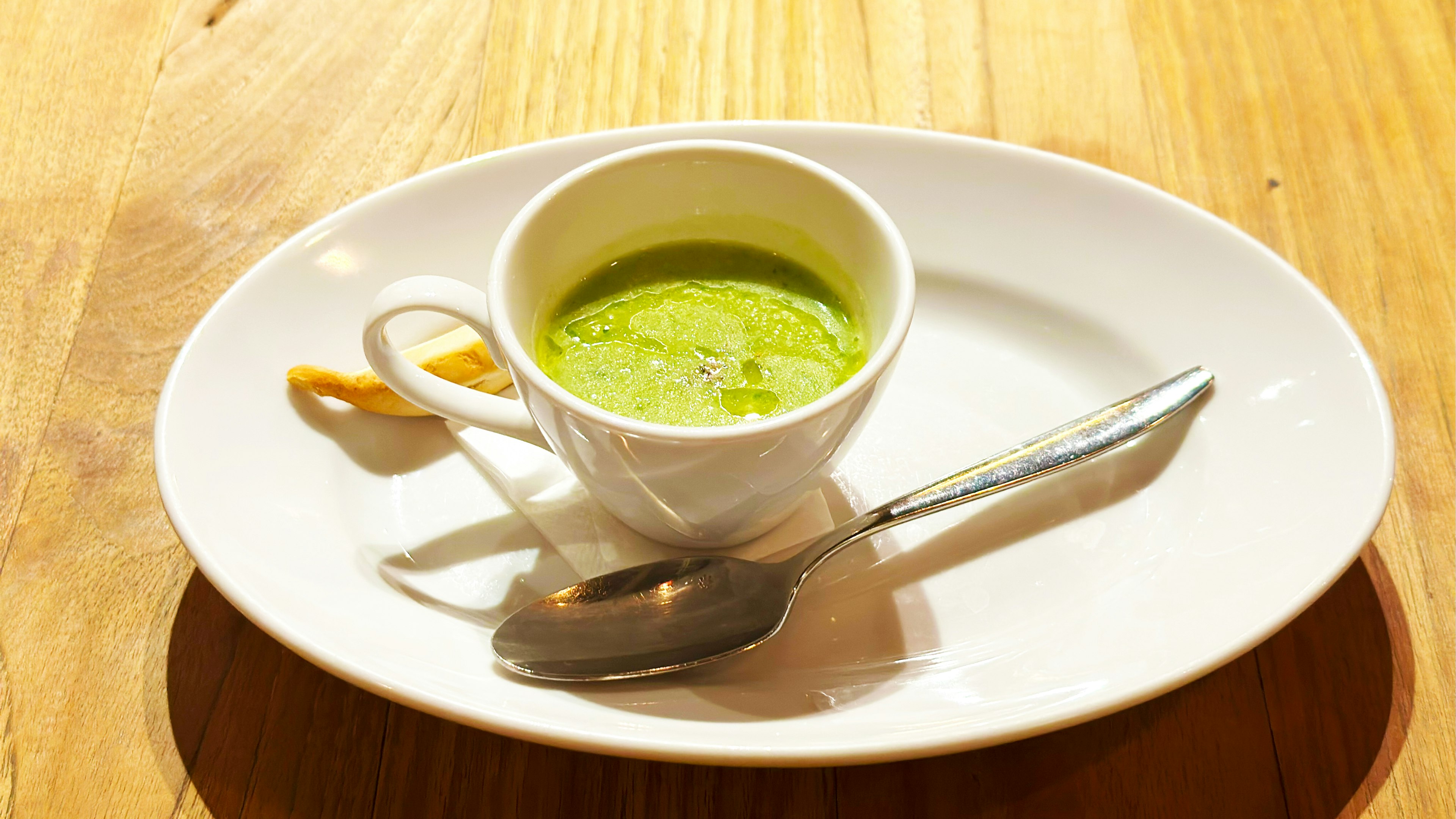 Green soup in a white cup on a plate with a spoon