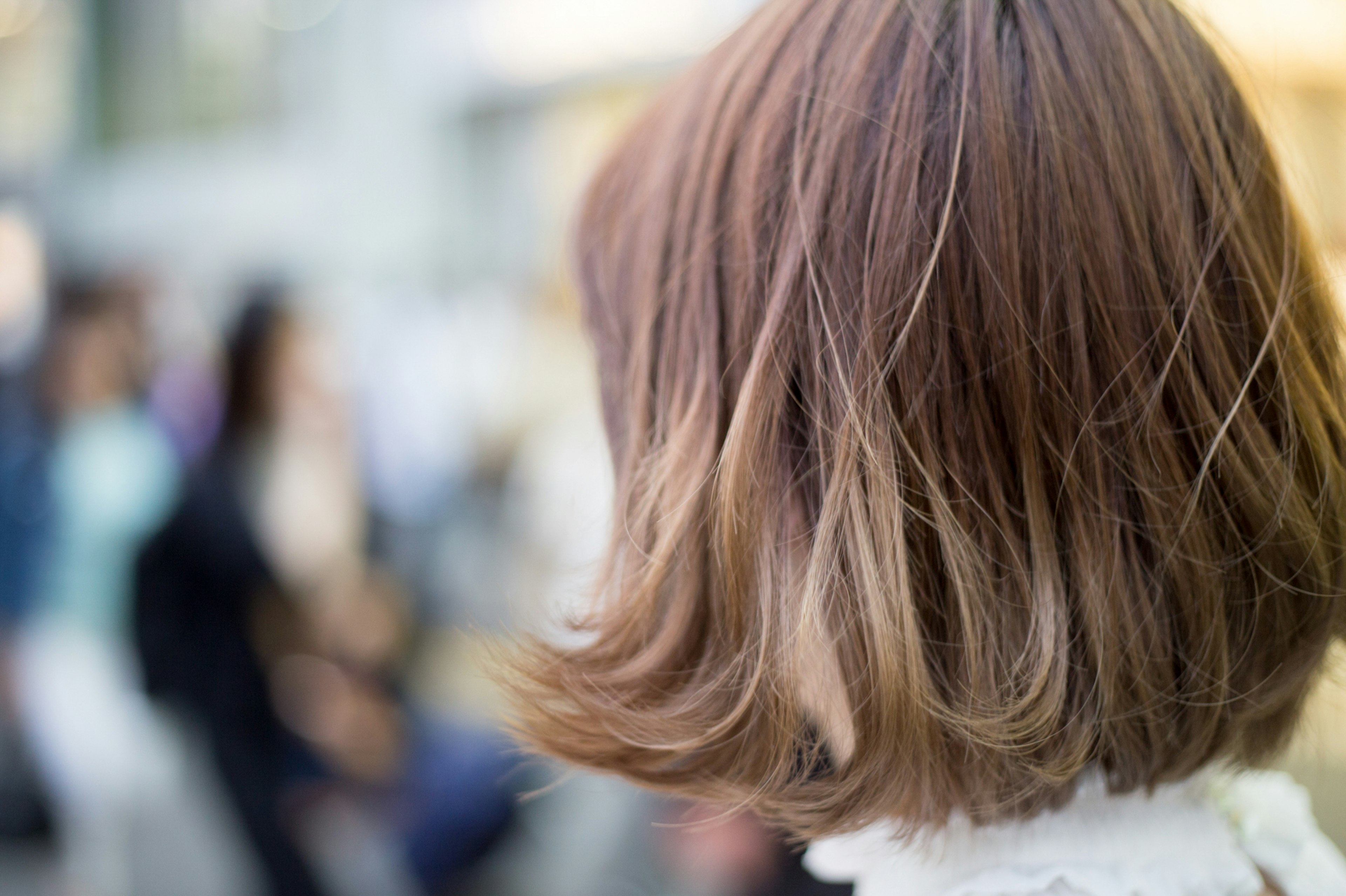 Woman with brown hair seen from the back with people in the background