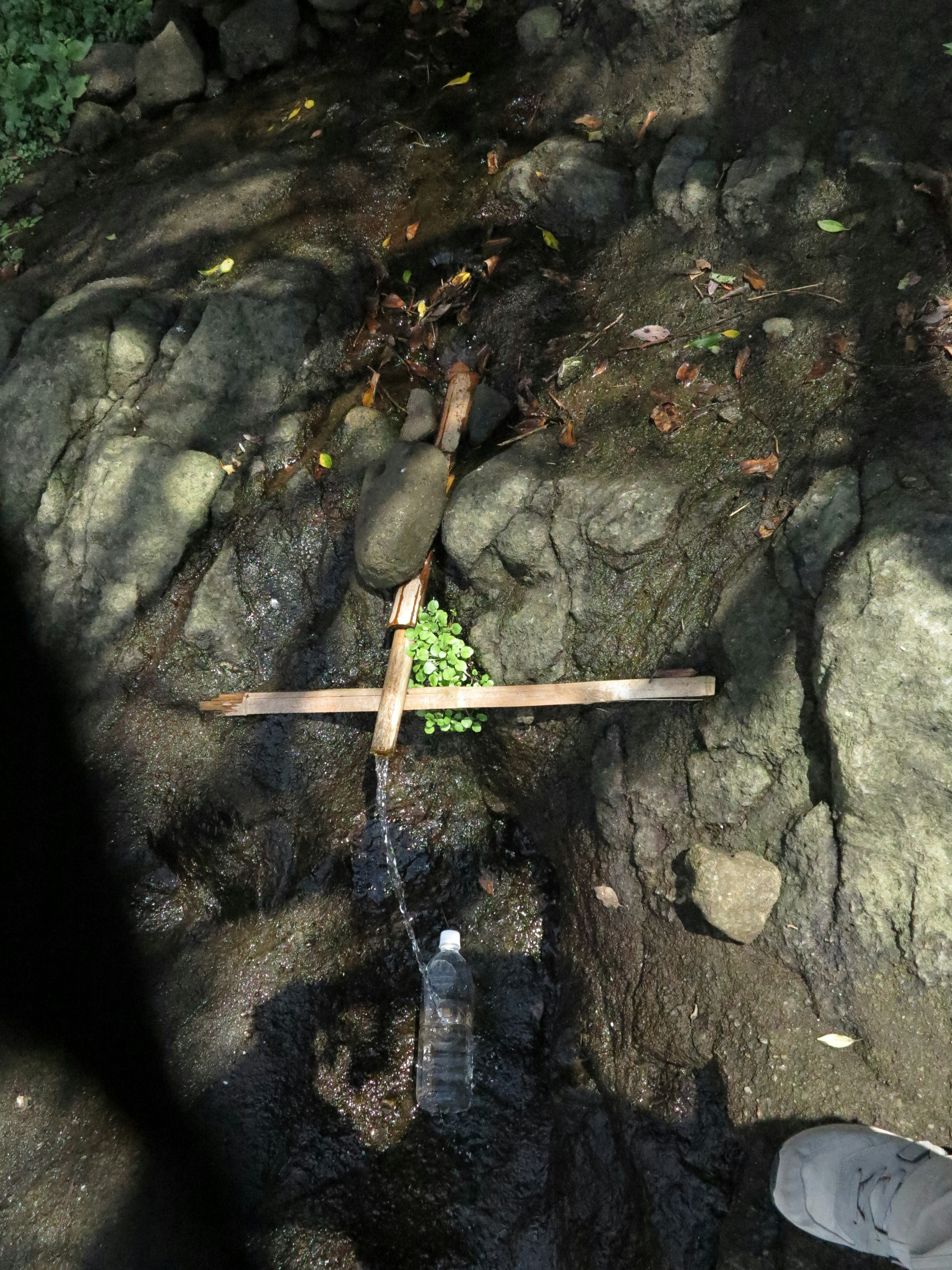 A wooden cross in a stream with flowing water and a plastic bottle