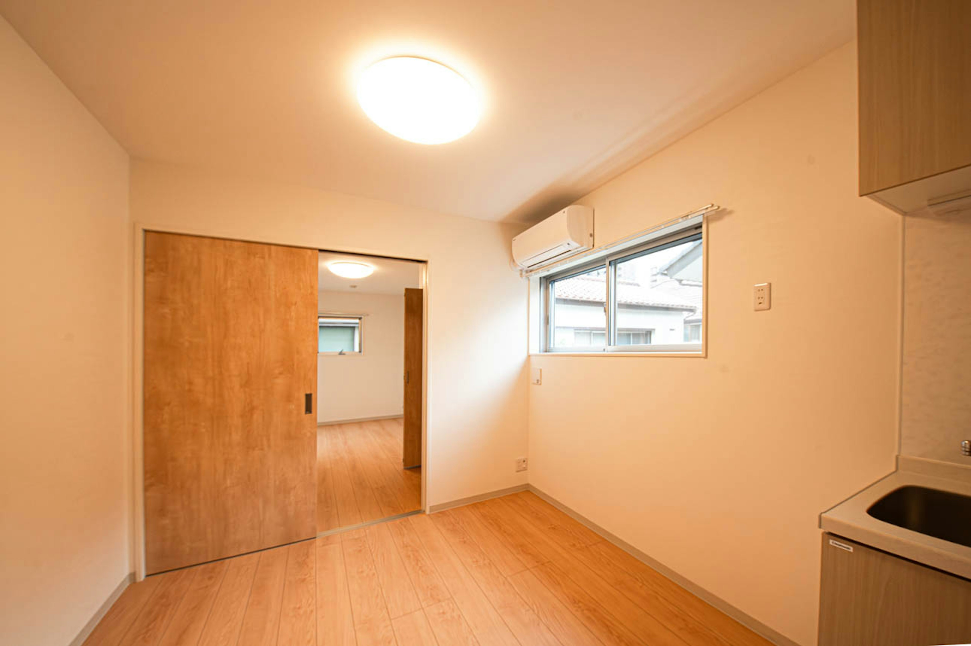 Habitación simple con paredes claras y suelo de madera con una ventana y una puerta