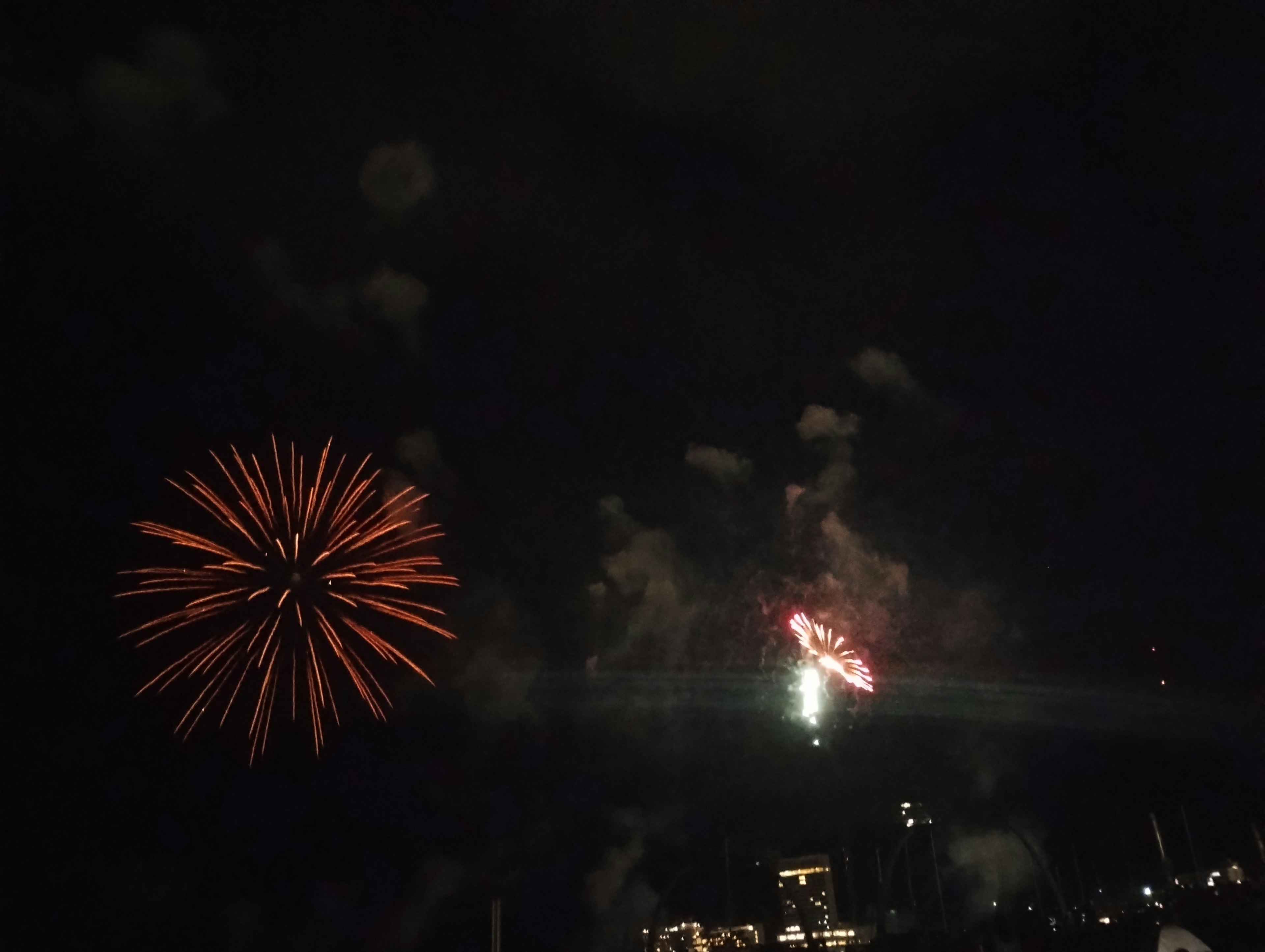 Fireworks display in the night sky featuring an orange firework and a central burst of light