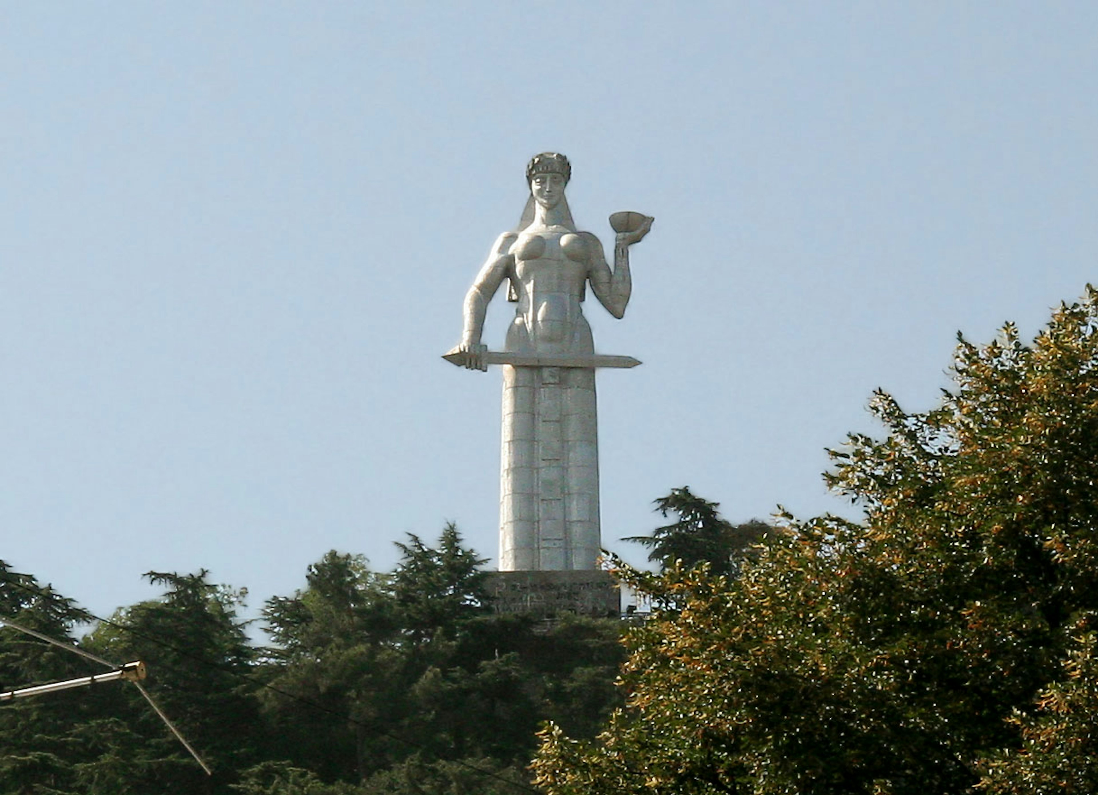 A large white statue stands on a hill holding a plate in one hand and raising the other