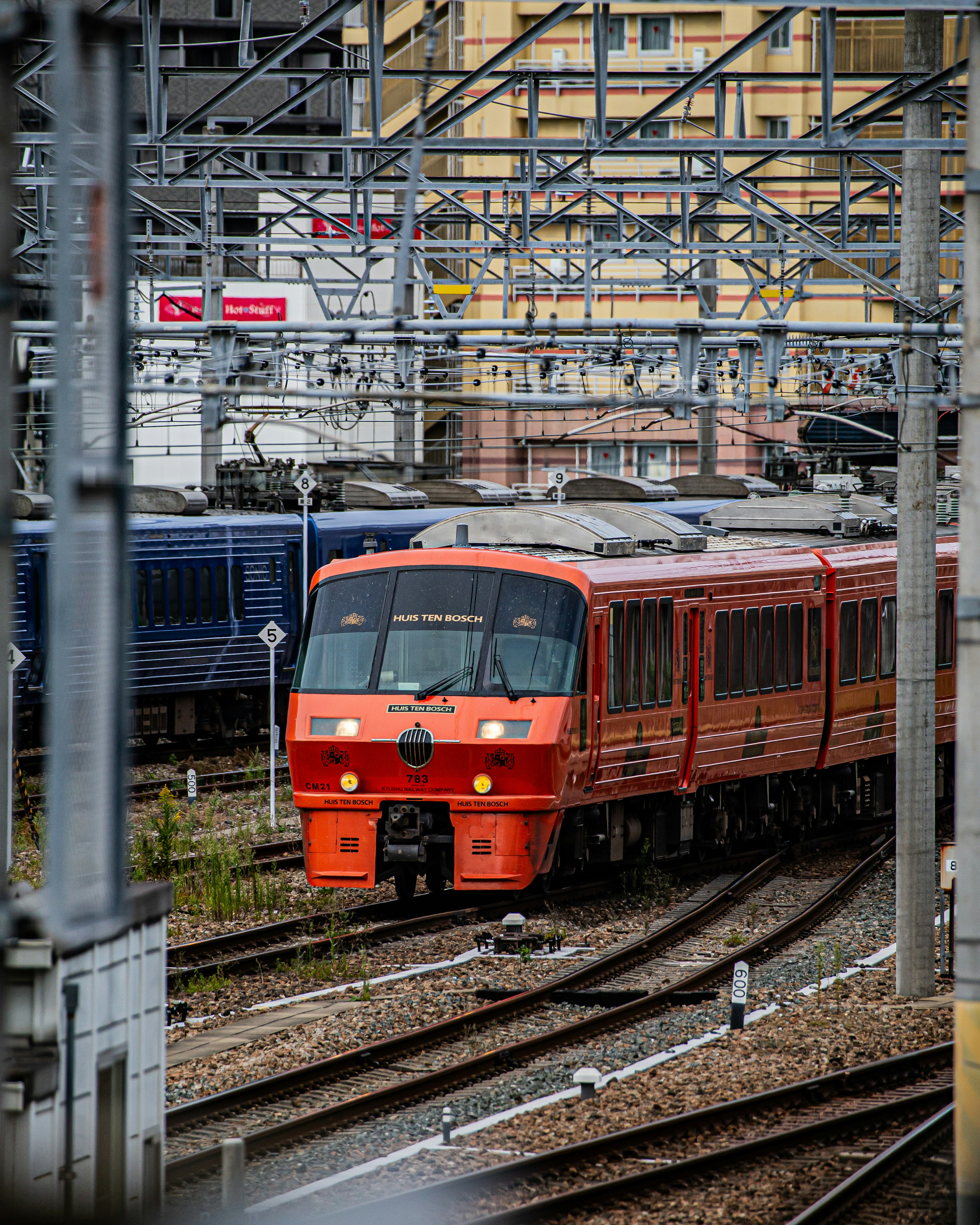 An orange train navigating railway tracks surrounded by structures